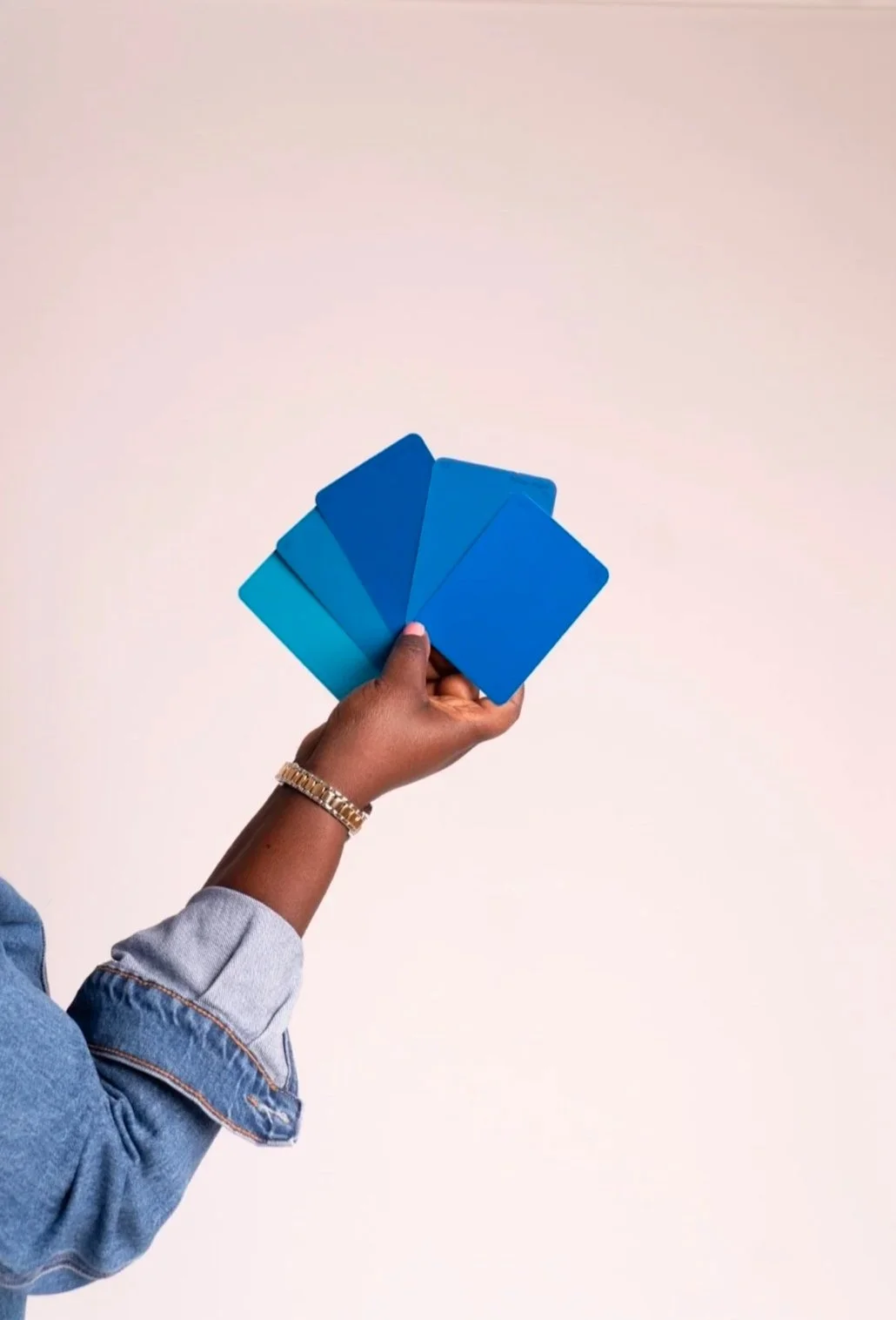 A person holding five blue color swatches or cards in their hand against a plain, light-colored background.