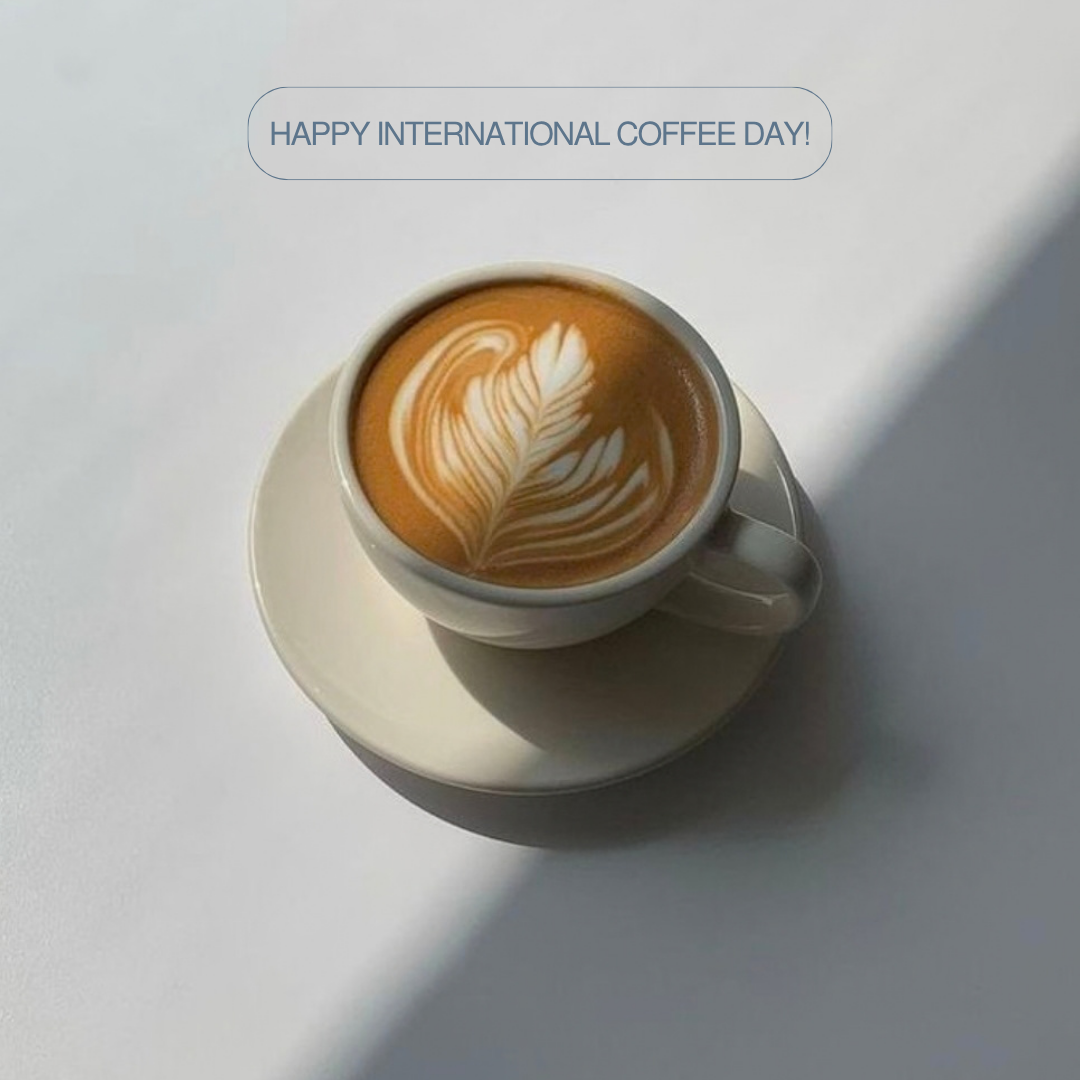 Latte art in a white coffee cup and saucer with “Happy International Coffee Day!” text