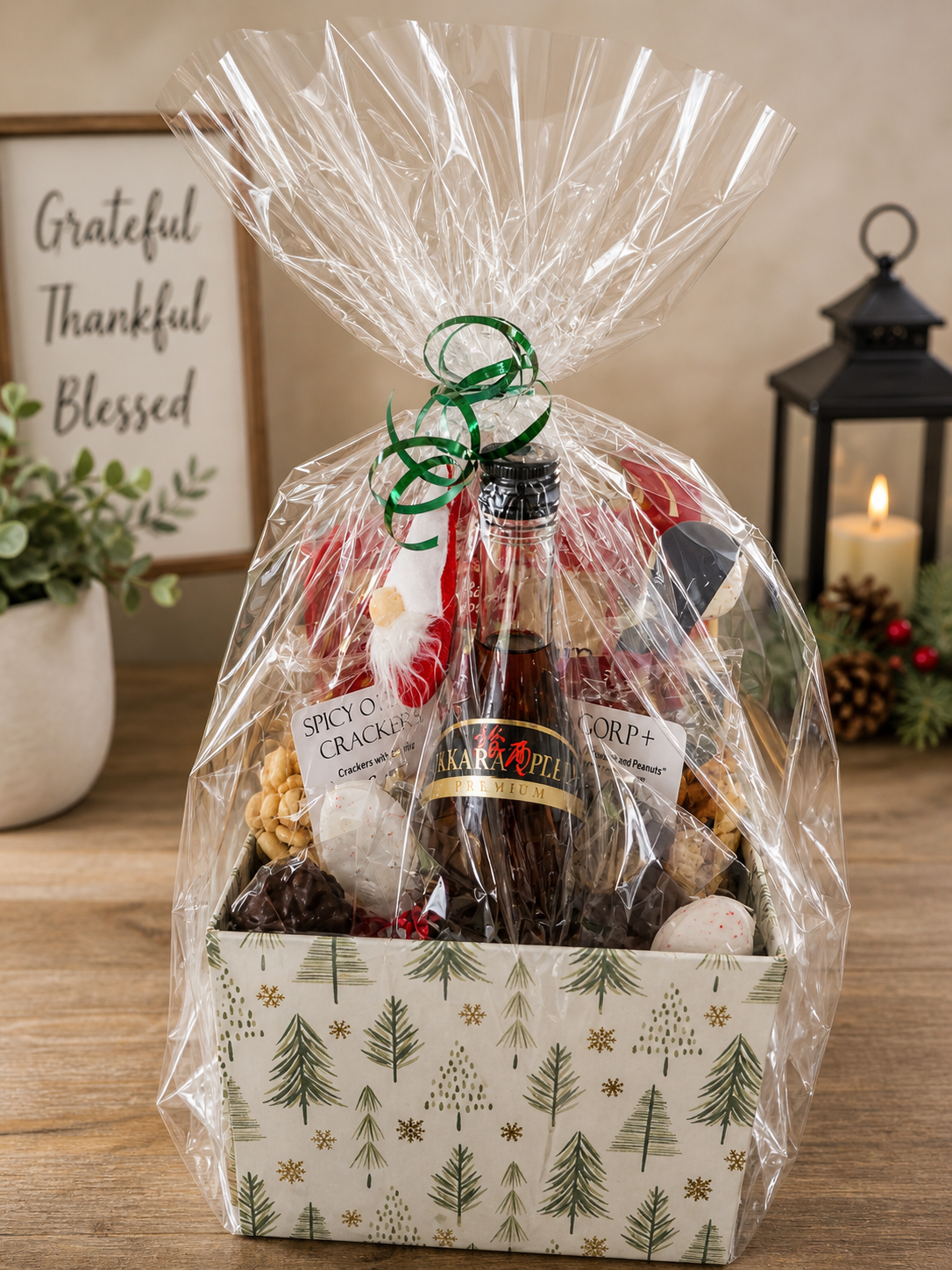 Gift basket wrapped in clear plastic with green ribbons, containing a bottle of Sparkle premium beer, assorted snacks, chocolates, and cookies, placed on a wooden surface.