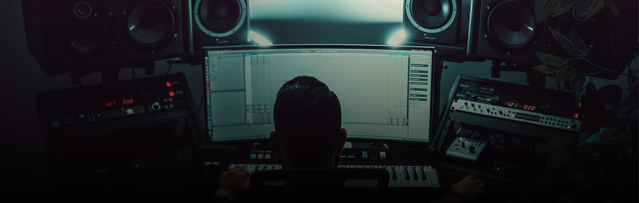 A person working on a music production computer setup with audio equipment and monitors in a dimly lit room.