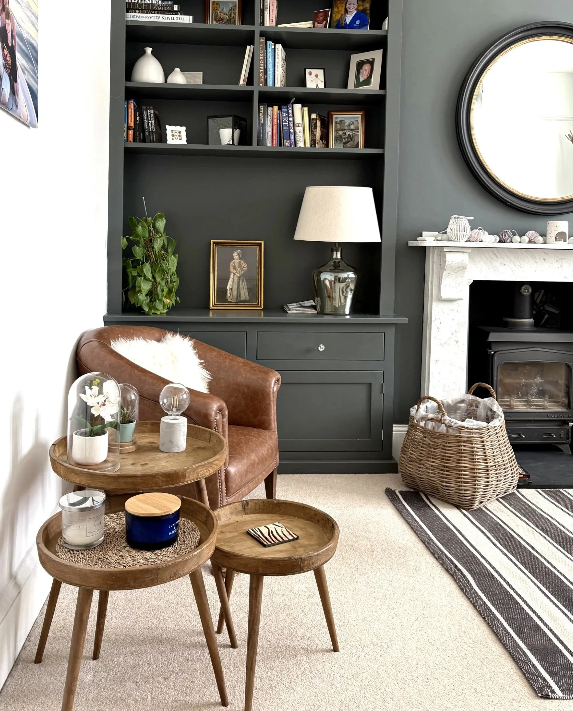 Layered living room with original marble fireplace, dark built-in cabinetry, circular mirror and wood burner