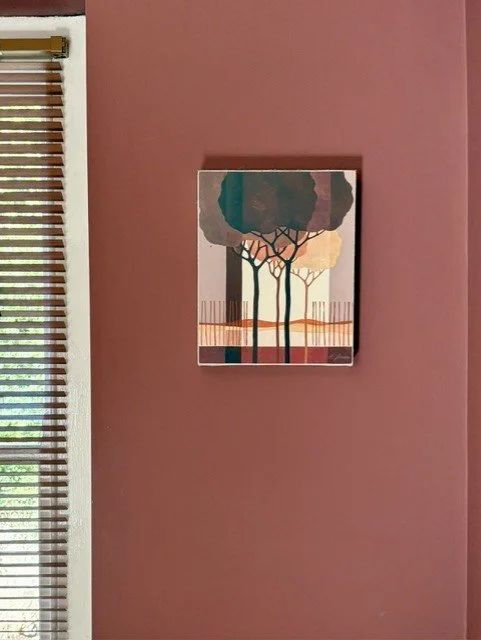 Coordinated artwork on a soft-red bathroom wall, echoing the horizontal lines of wooden slatted blinds