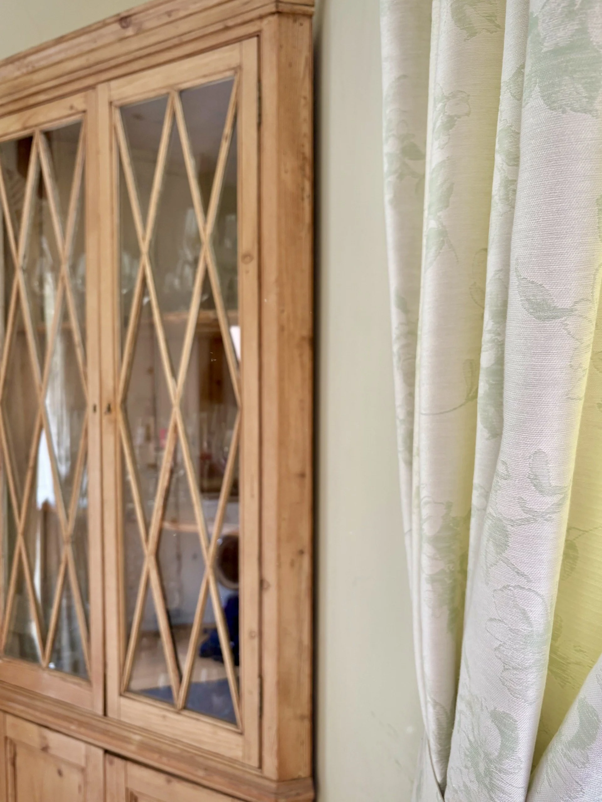 Kitchen corner blending delicately patterned curtains with an antique glazed cupboard, combining muted colour, texture and heritage detail