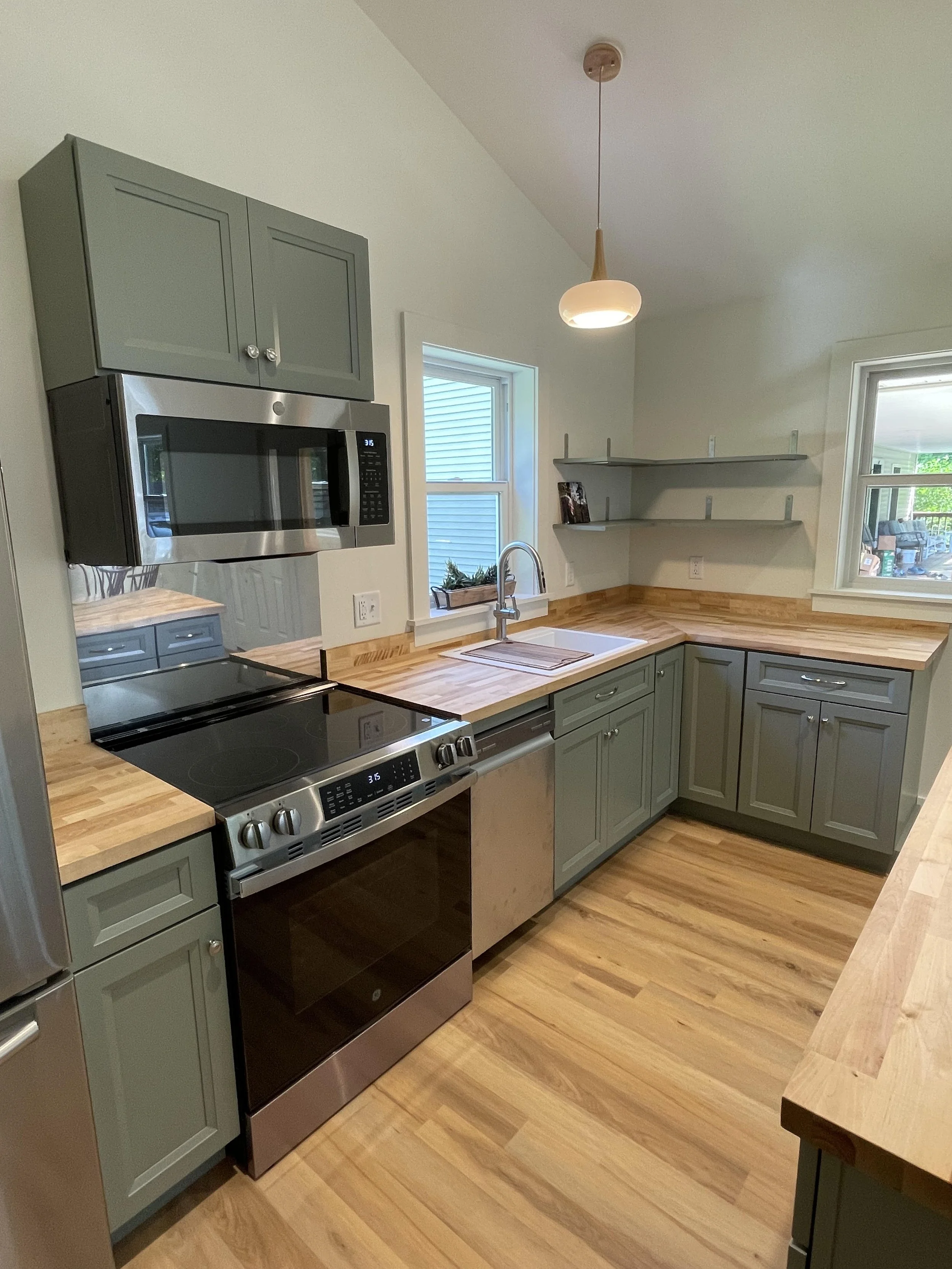 Kitchen with green cabinets, wooden countertops, stainless steel oven, microwave, and hardwood flooring, with windows showing outdoor patio furniture.