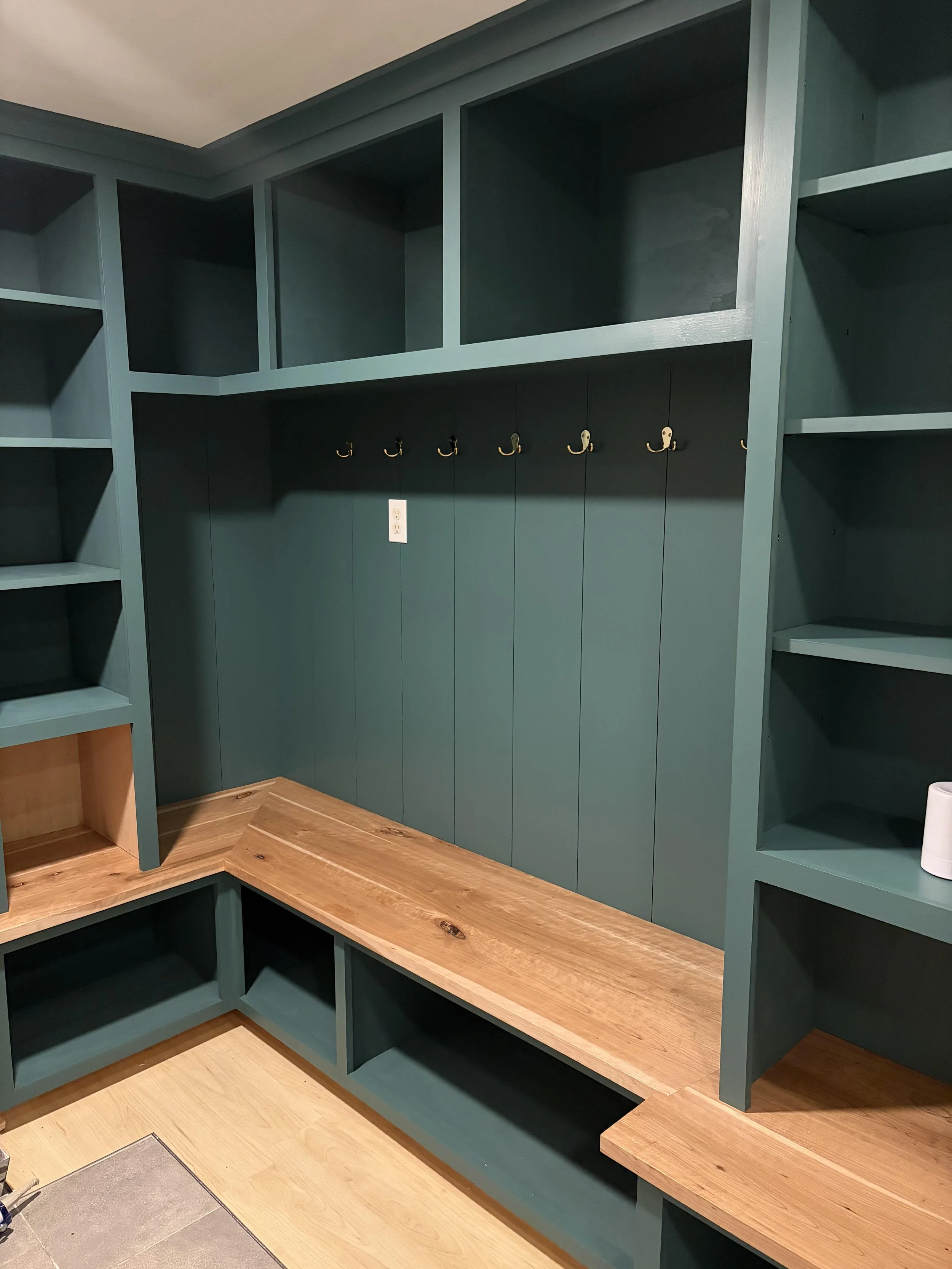 Custom-built teal-colored wall storage with open shelves and hooks, featuring a natural wood countertop and flooring.