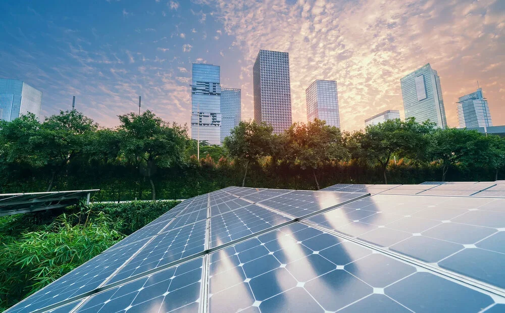 Solar panels in the foreground with city skyscrapers and a sunset sky in the background.
