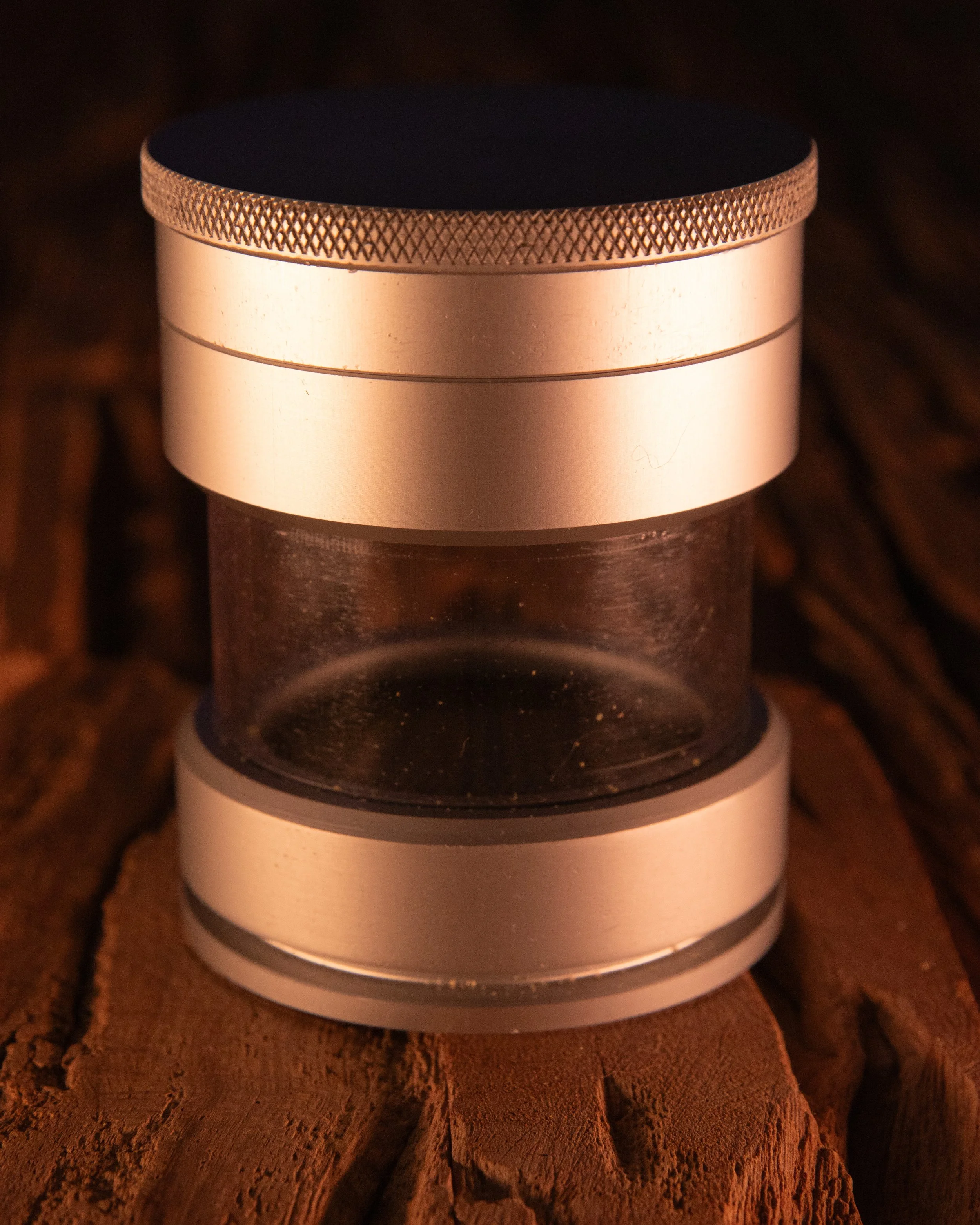 Close-up of a metal cylindrical object with textured edges, placed on rough, reddish-brown wood.