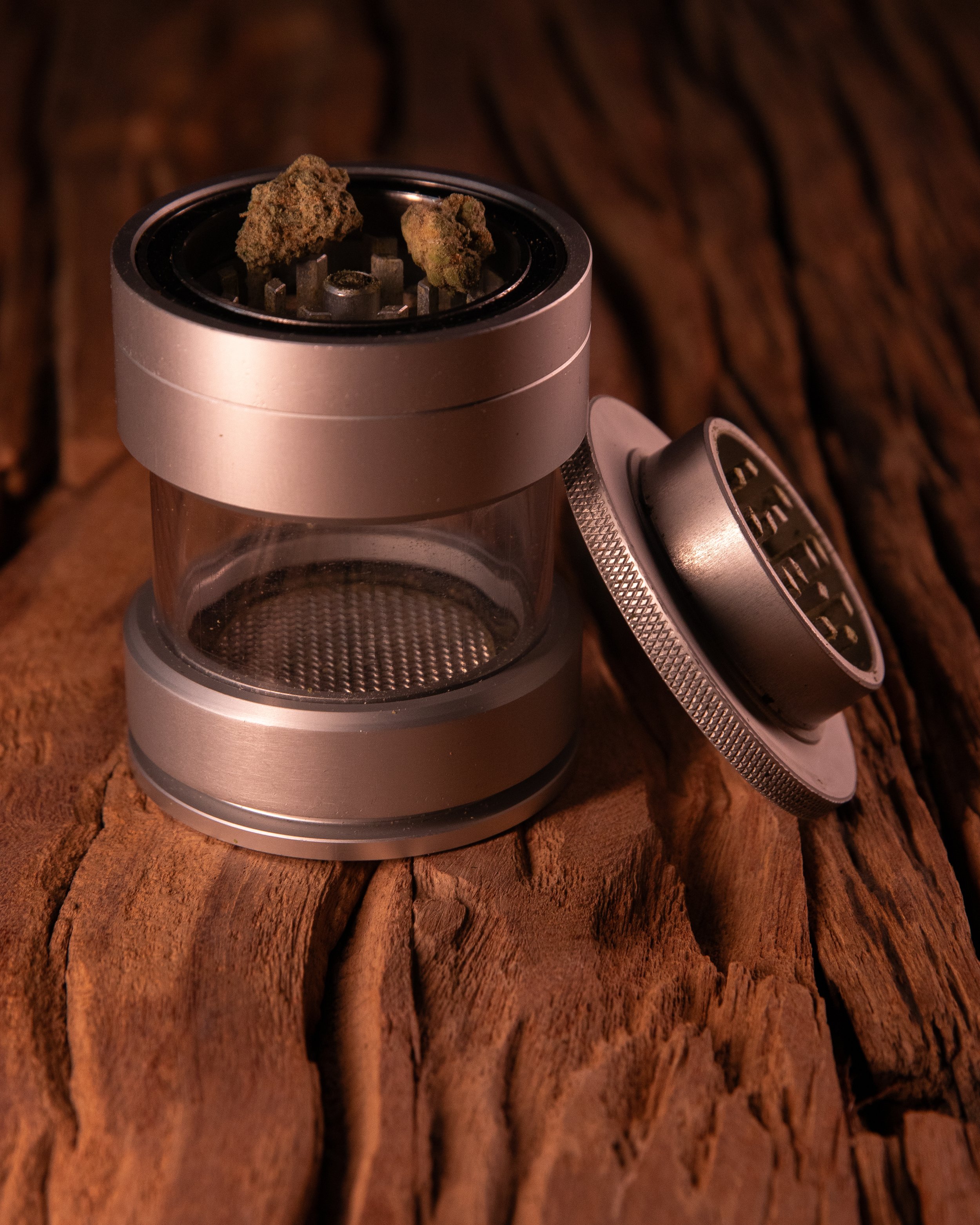 A weed grinder with two cannabis buds on top, placed on a rough wooden surface.