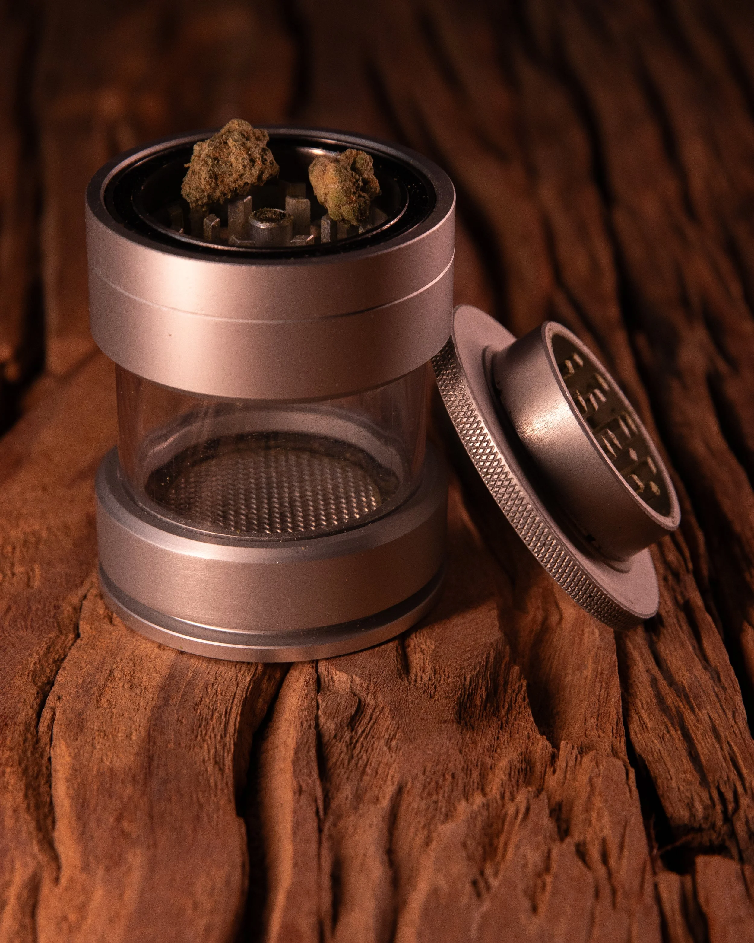 A weed grinder with two cannabis buds on top, placed on a rough wooden surface.