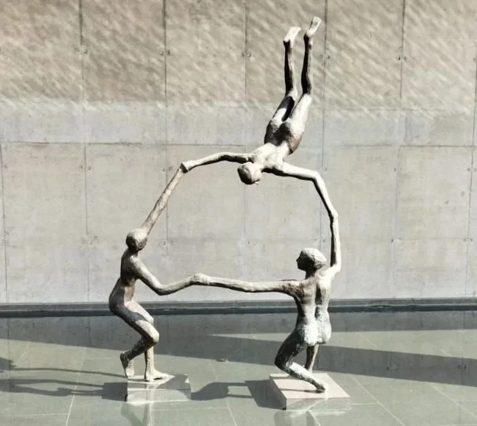 Sculpture of three human figures holding hands, with one figure upside down above the others, forming a circular shape.