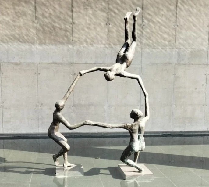 Sculpture of three human figures holding hands, with one figure upside down above the others, forming a circular shape.