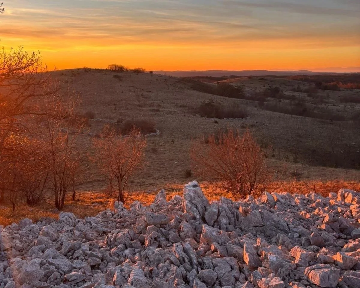 Sunset over the Adriatic countryside, with warm light illuminating rolling hills and natural landscape.
