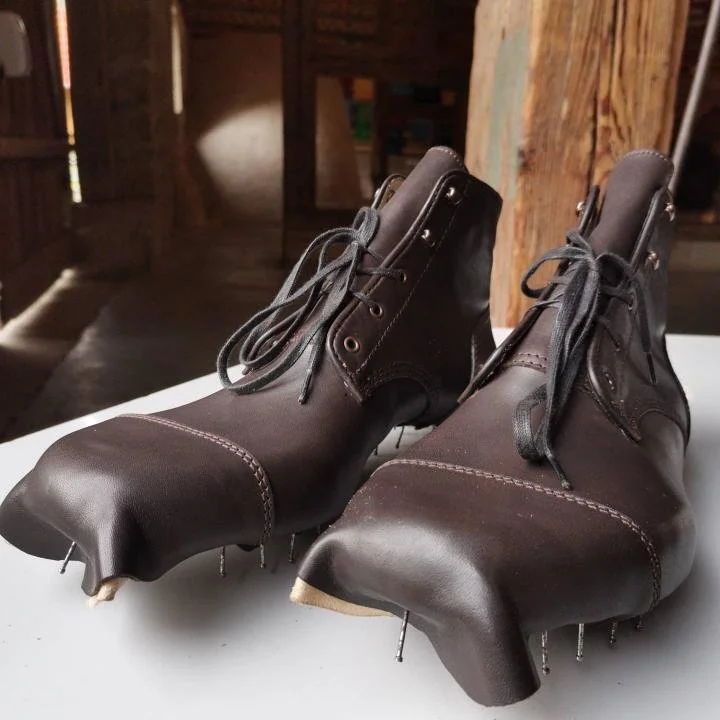 Ein Paar schwarze Tanzschuhe mit Absätzen auf weißem Untergrund, die an den Zehen und Absätzen mit Reißzwecken befestigt sind.