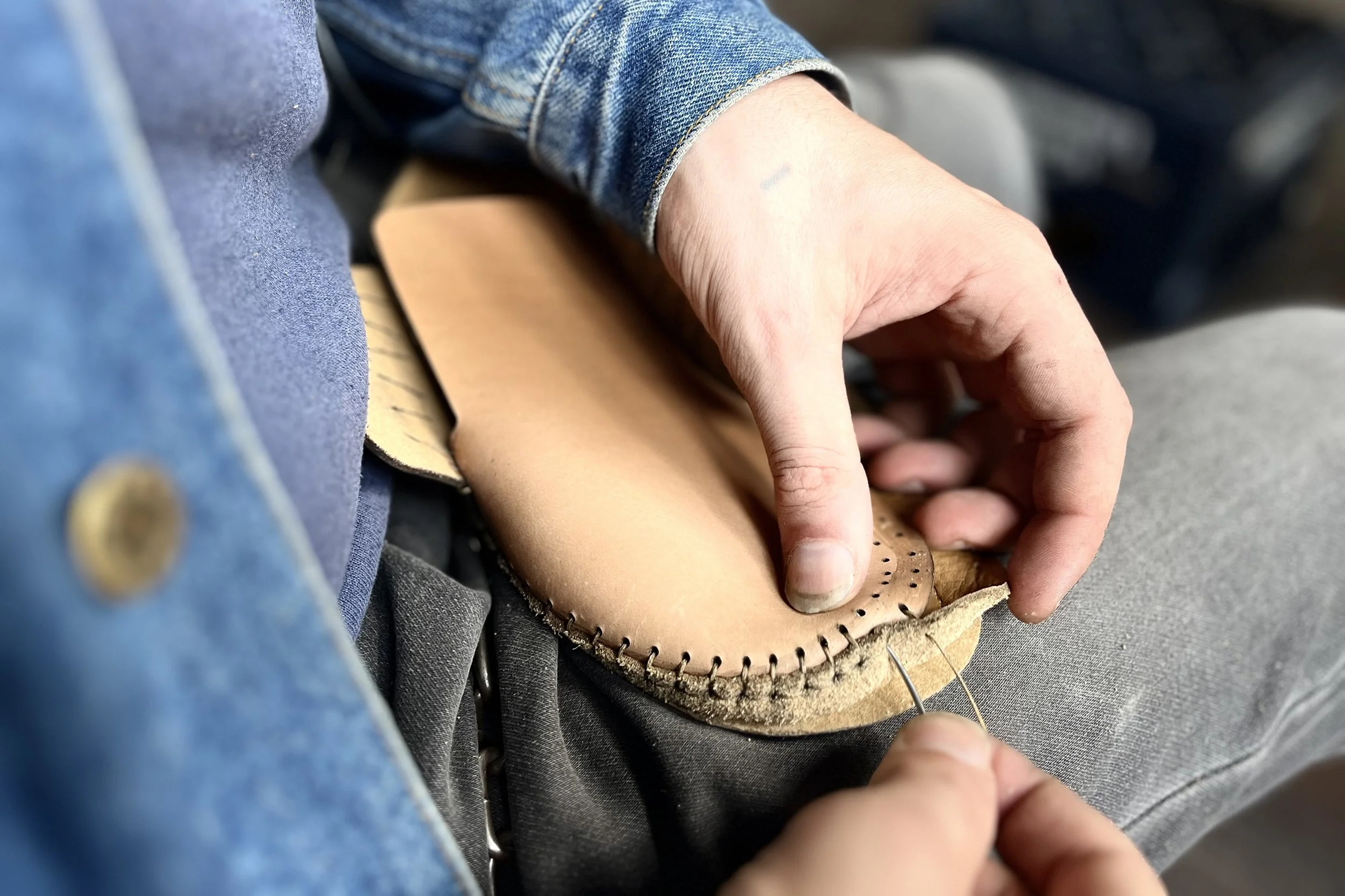 Hand bearbeitet ein ledernes Schuhstück, wahrscheinlich beim Schuhmacher oder Lederwarenhersteller.