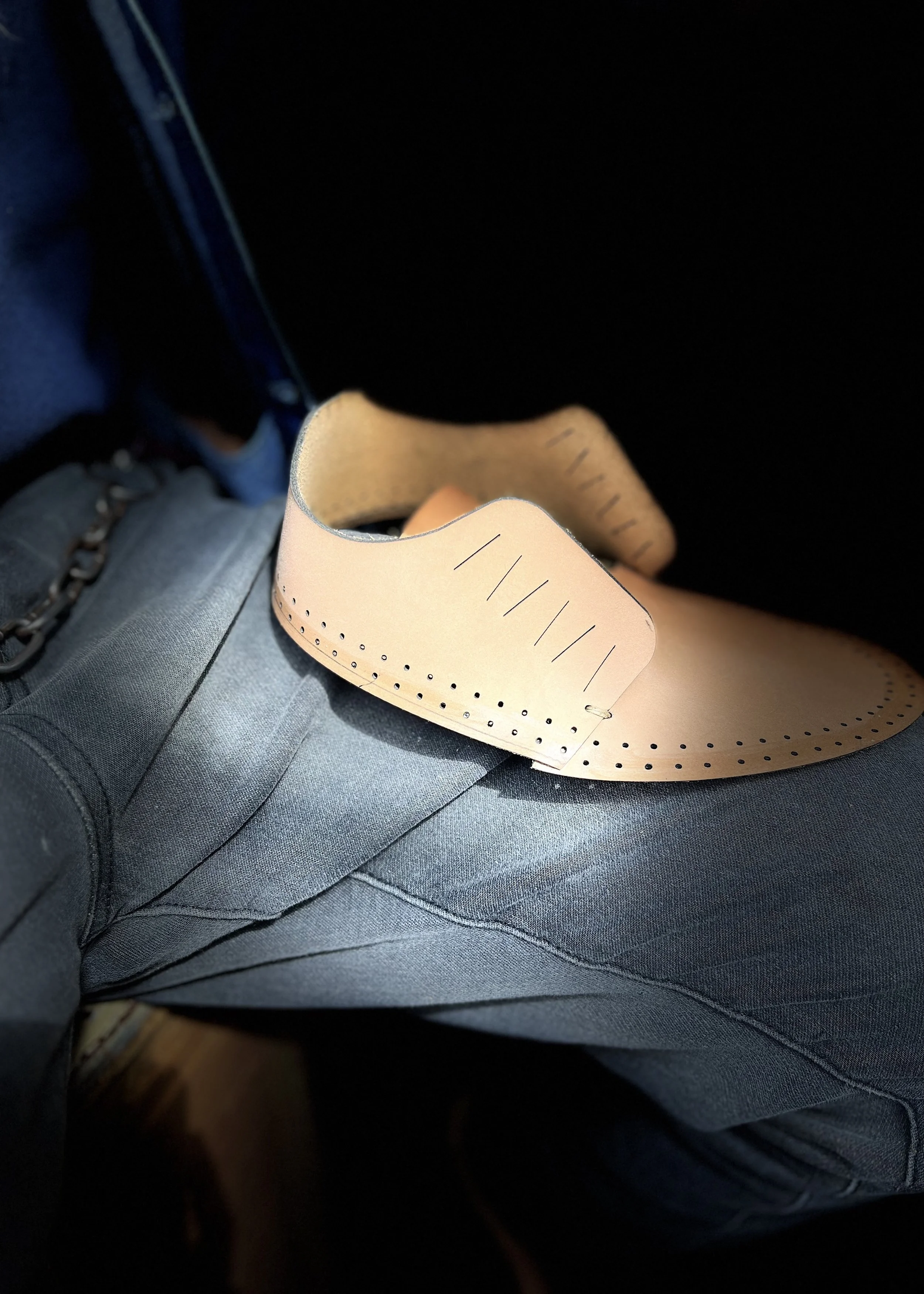 Nahaufnahme eines Fußes mit einem gepolsterten Riemen, wahrscheinlich einer orthopädischen Schiene, in einem Kleidungsstück, das Jeans ähnelt, vor einem dunklen Hintergrund.