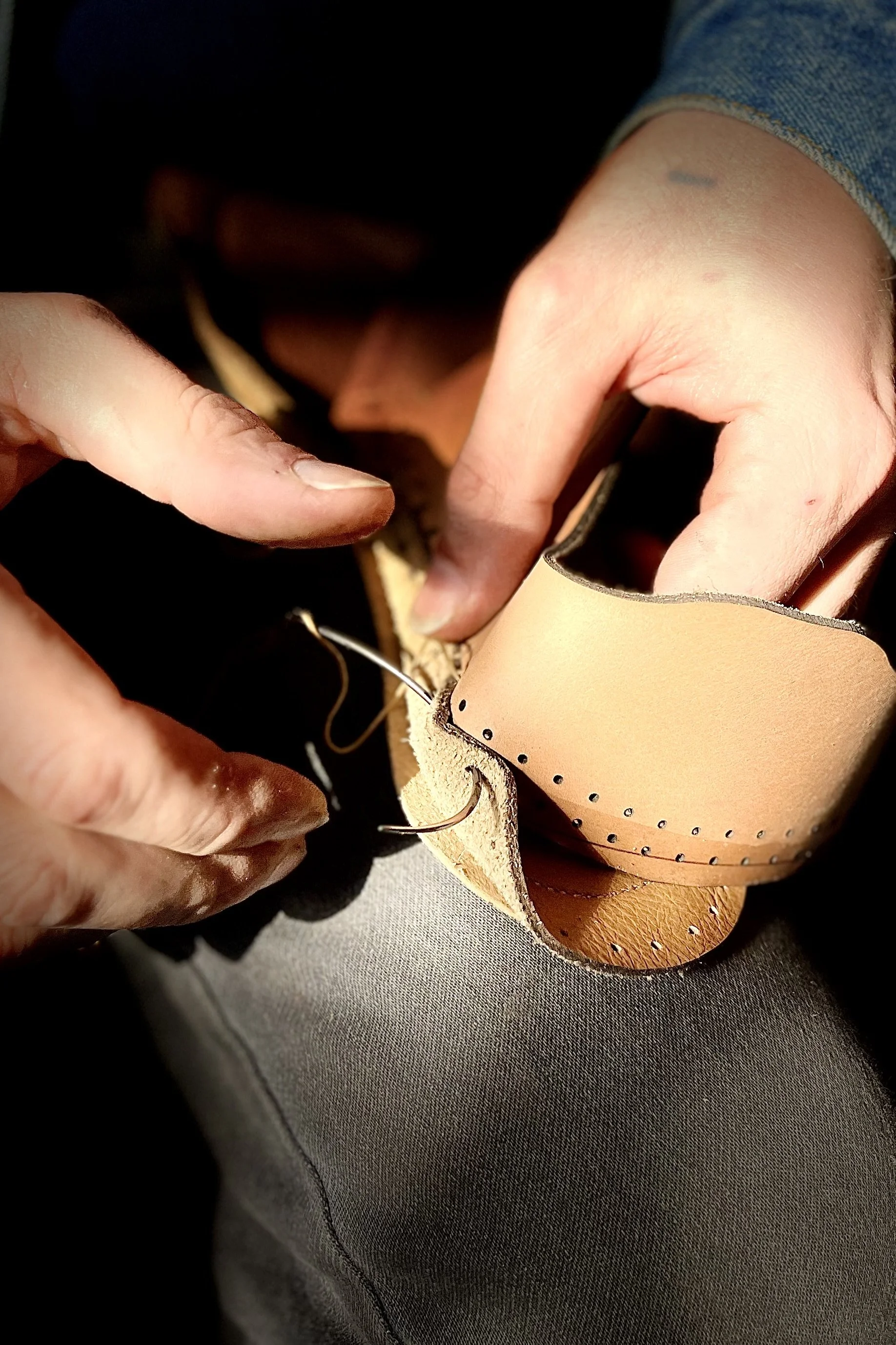 Nahaufnahme von Händen, die an einem Schuh arbeiten, möglicherweise beim Nähen oder Reparieren eines Lederschuhs.