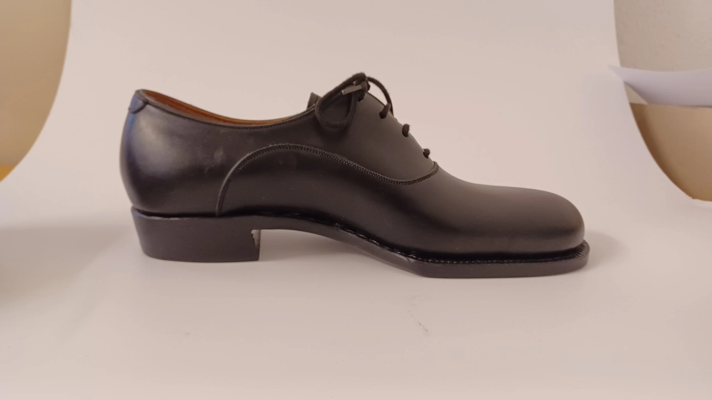 Schwarzes Lederpaar Schuhe mit dickem Absatz, auf einer weißen Oberfläche gemessen.