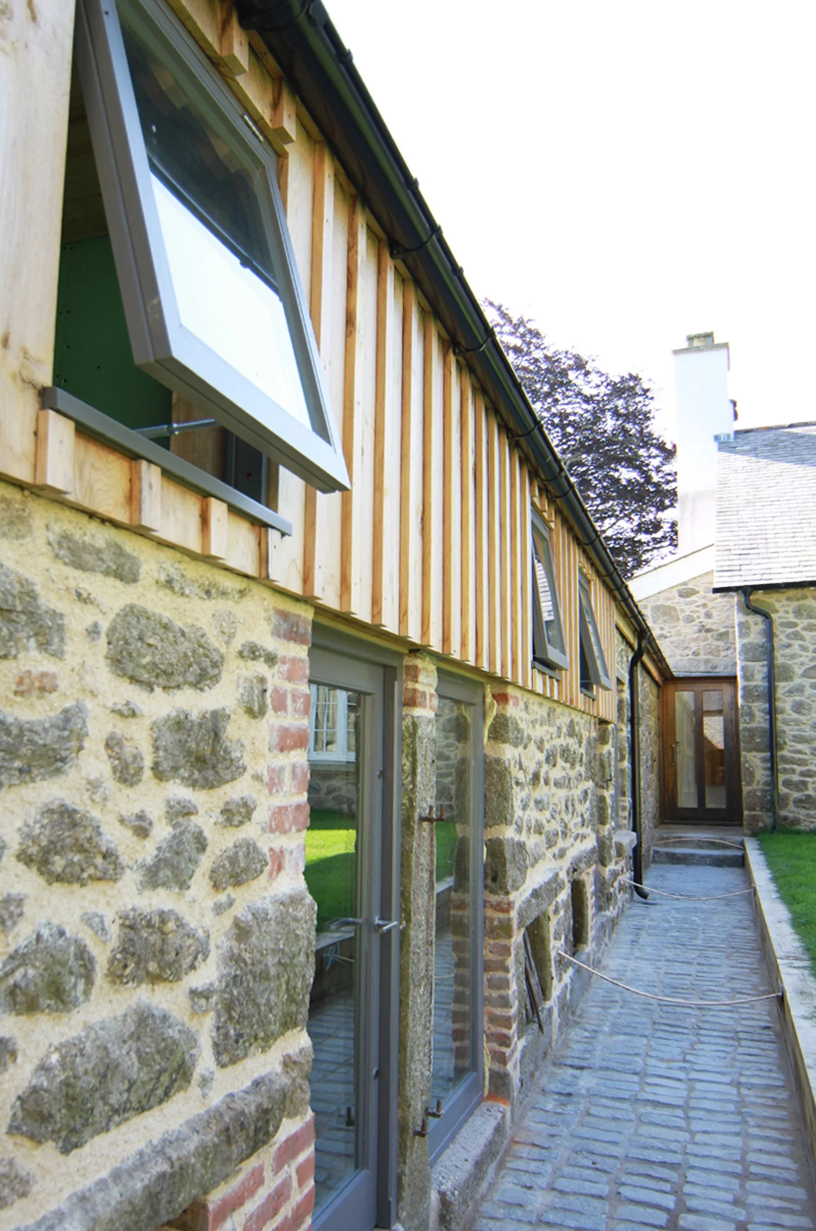 Levitate Architects Torhill Farm heritage architecture featuring restored stone walls, timber cladding, and cobbled path linking farmhouse and barns.