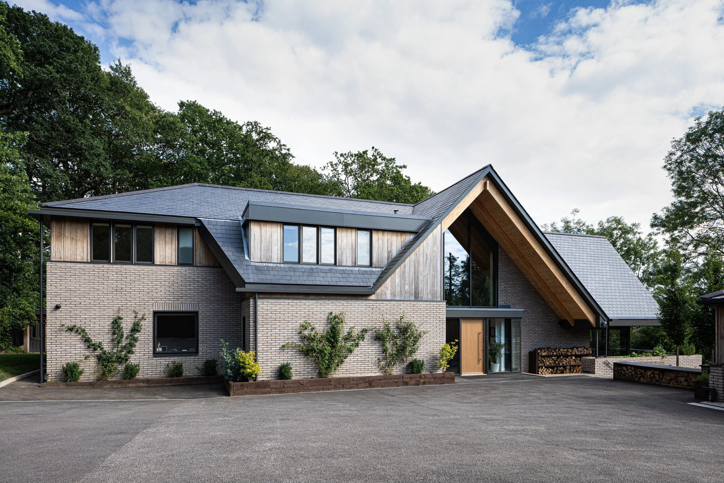 Levitate Architects' Highoaks: The front entrance of the modern two-story residence, displaying light-colored brickwork, timber cladding, and ivy trailing up the walls.