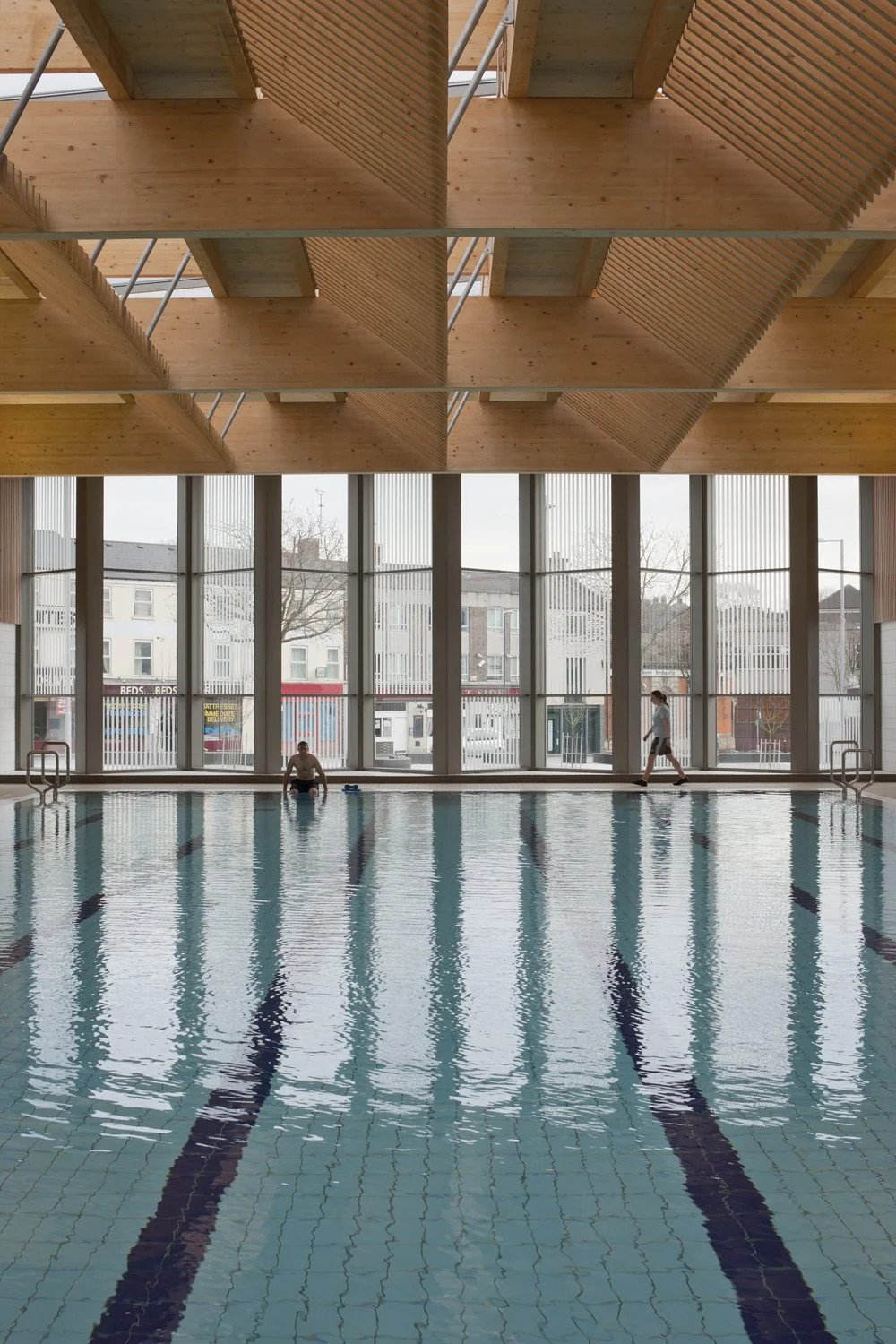 Levitate Architects' Victoria Leisure Centre: A clean, symmetrical view down the swimming lanes of the main pool, highlighting the massive floor-to-ceiling windows and timber ceiling architecture.