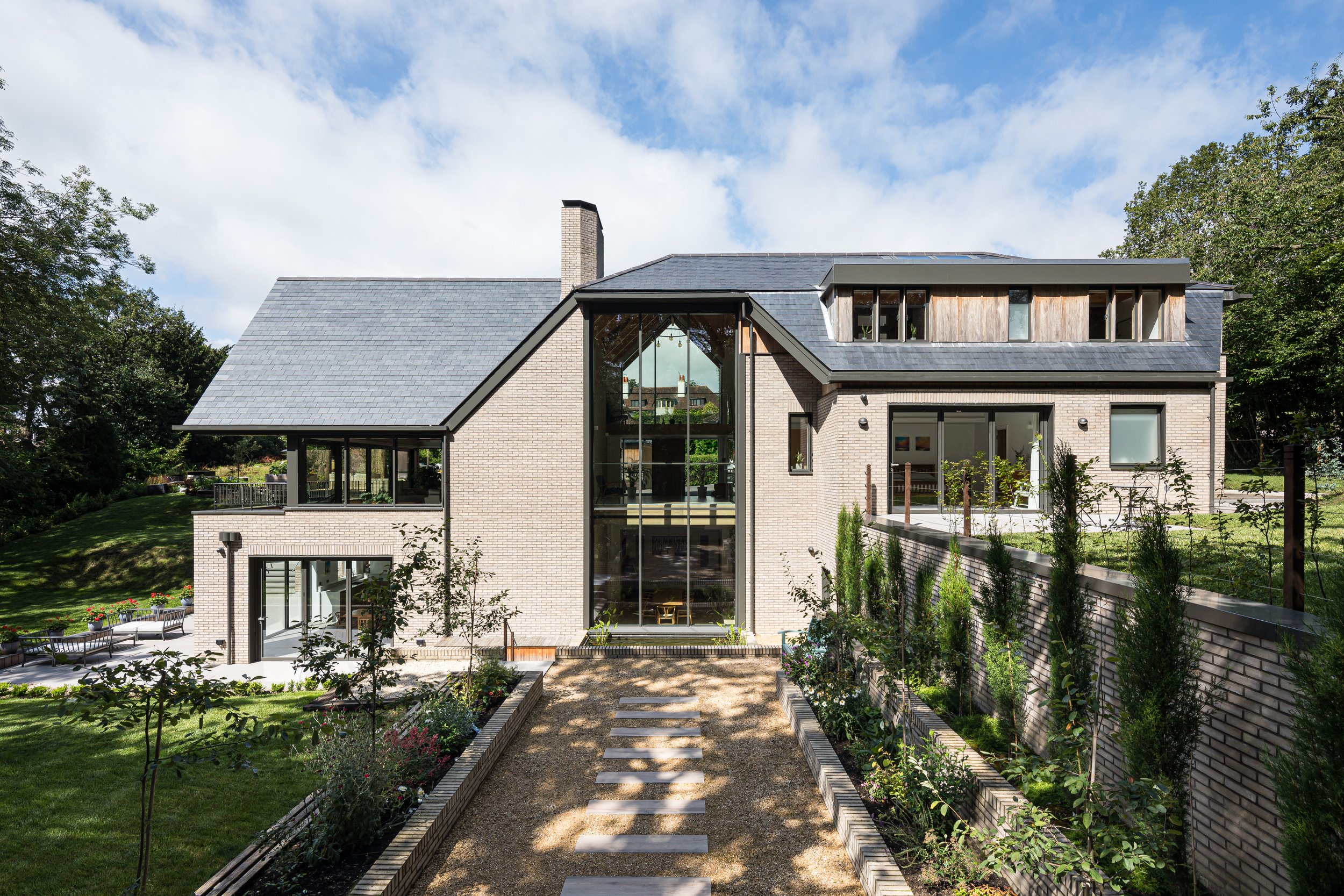 Levitate Architects' Highoaks: A symmetrical view of the grand rear exterior, featuring a central gravel pathway lined with low brick walls, neat green lawns, and manicured shrubbery.