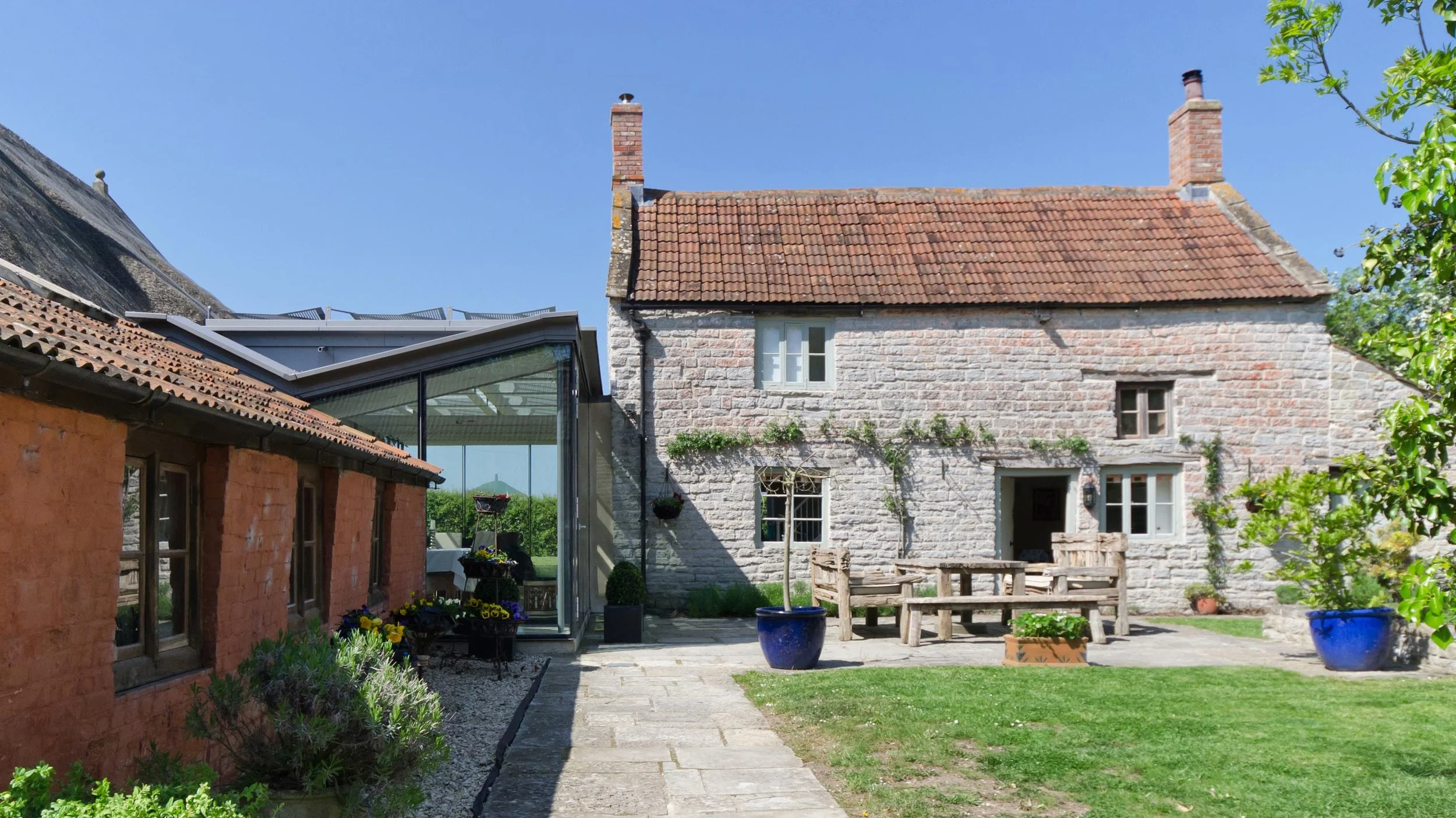 Award Winning Old Farm by Levitate Architects, courtyard view juxtaposing historic cottage stone walls with a sleek, modern glass extension.