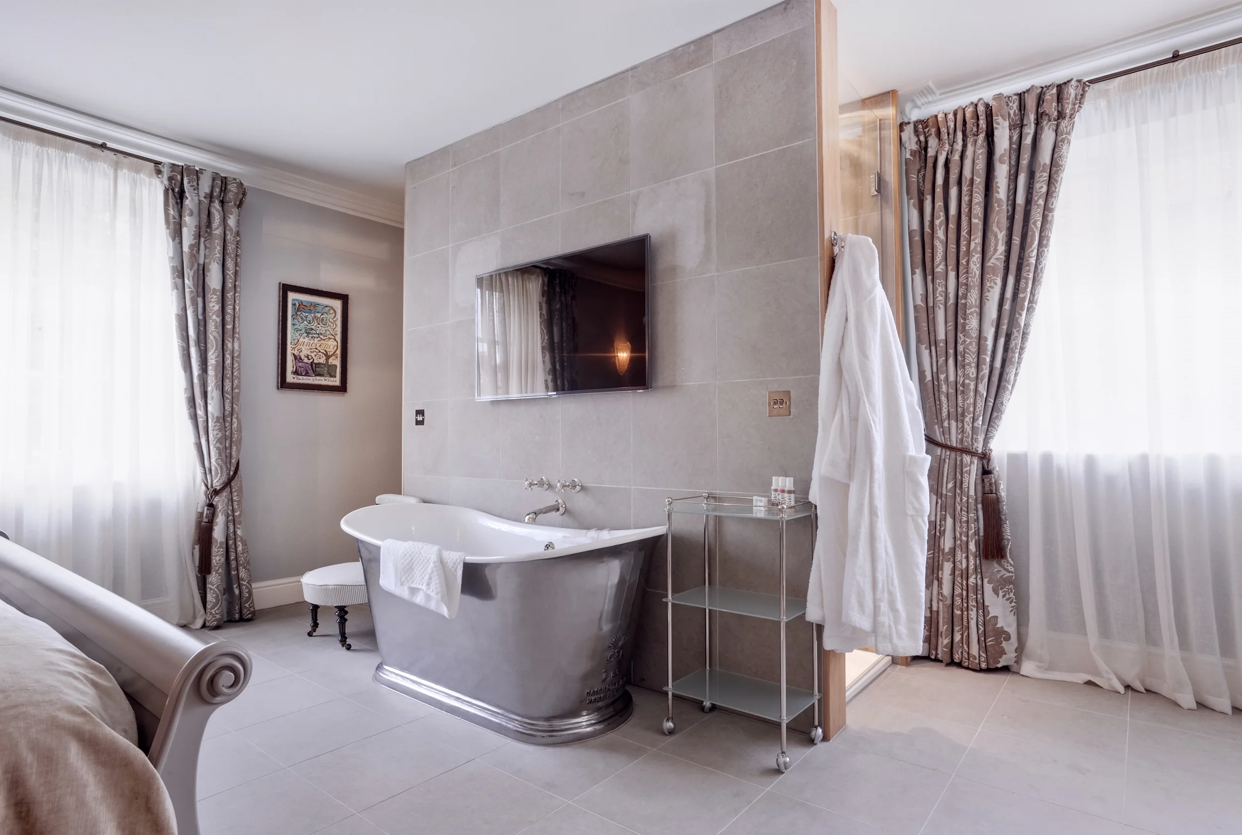 Levitate's Southernhay Hotel bedroom with an open plan polished bathtub set beside floral curtained windows