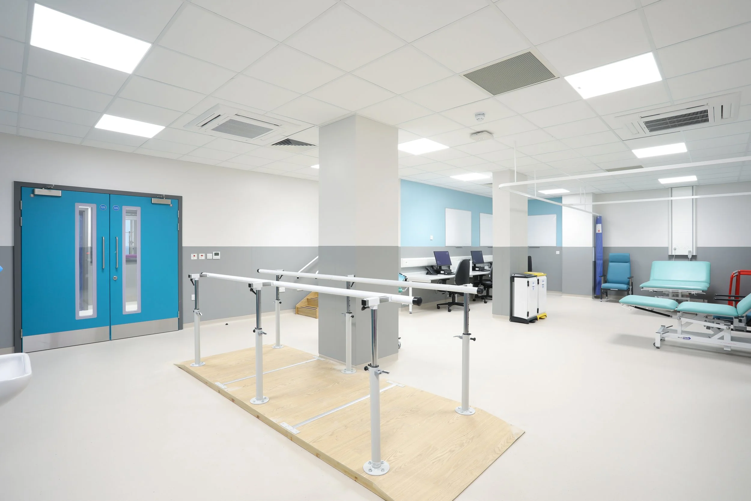 Hospital corridor with blue double doors, reclining chairs, medical equipment, and inspection platform.