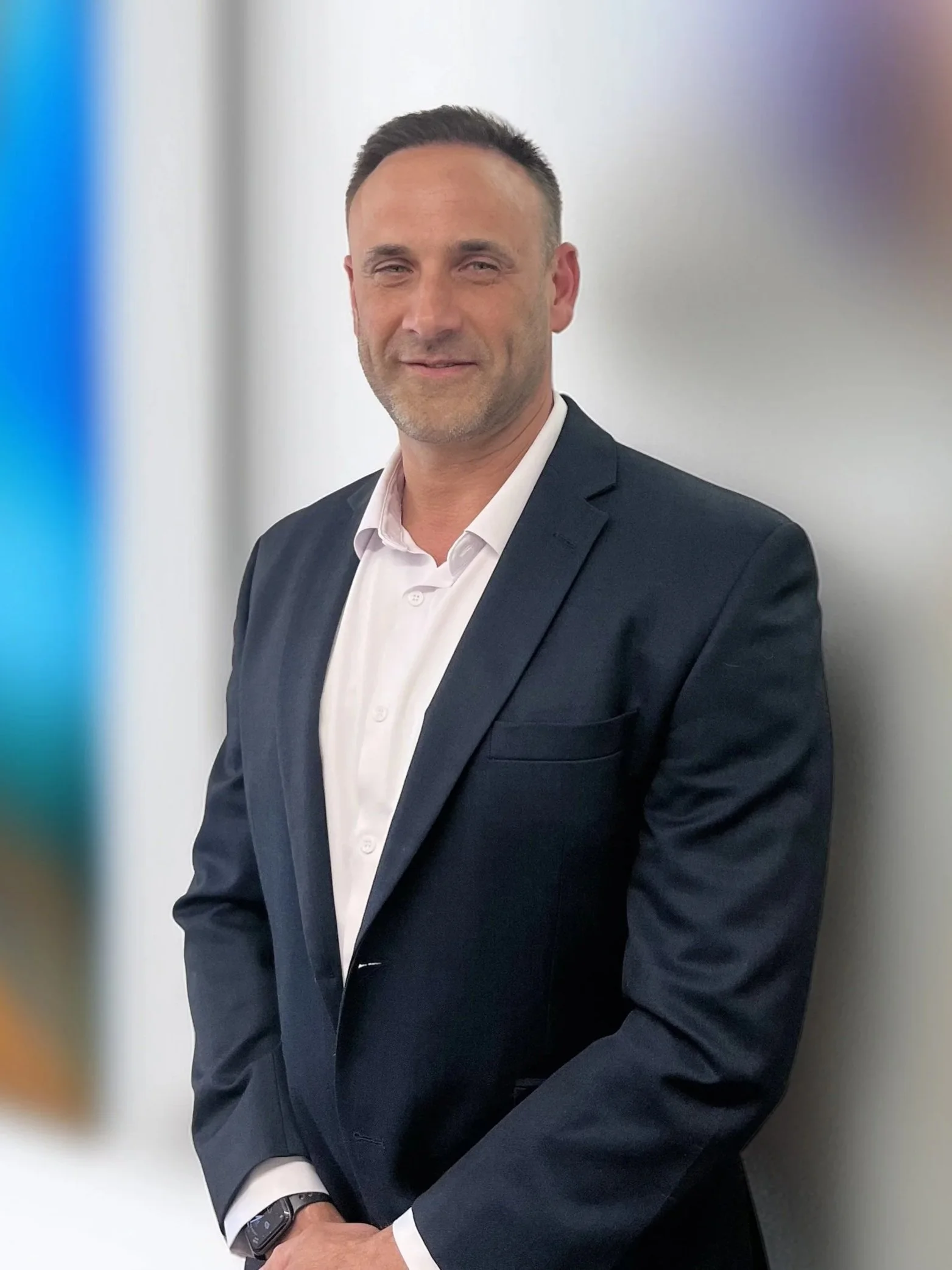 Portrait of a middle-aged man in a dark suit and white shirt, standing against a neutral background.