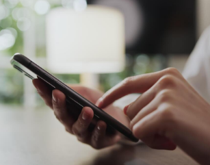 Person using smartphone at a desk with a blurred background.