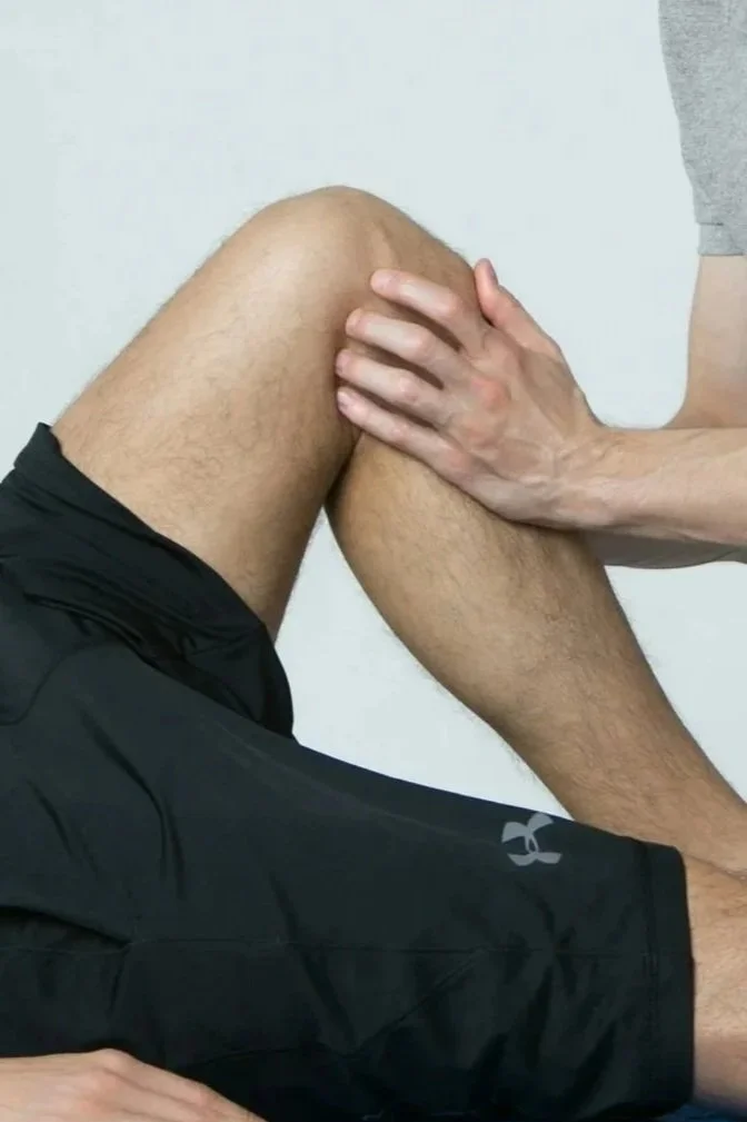 A person with knee pain in black shorts sitting while osteopath holds their knee.