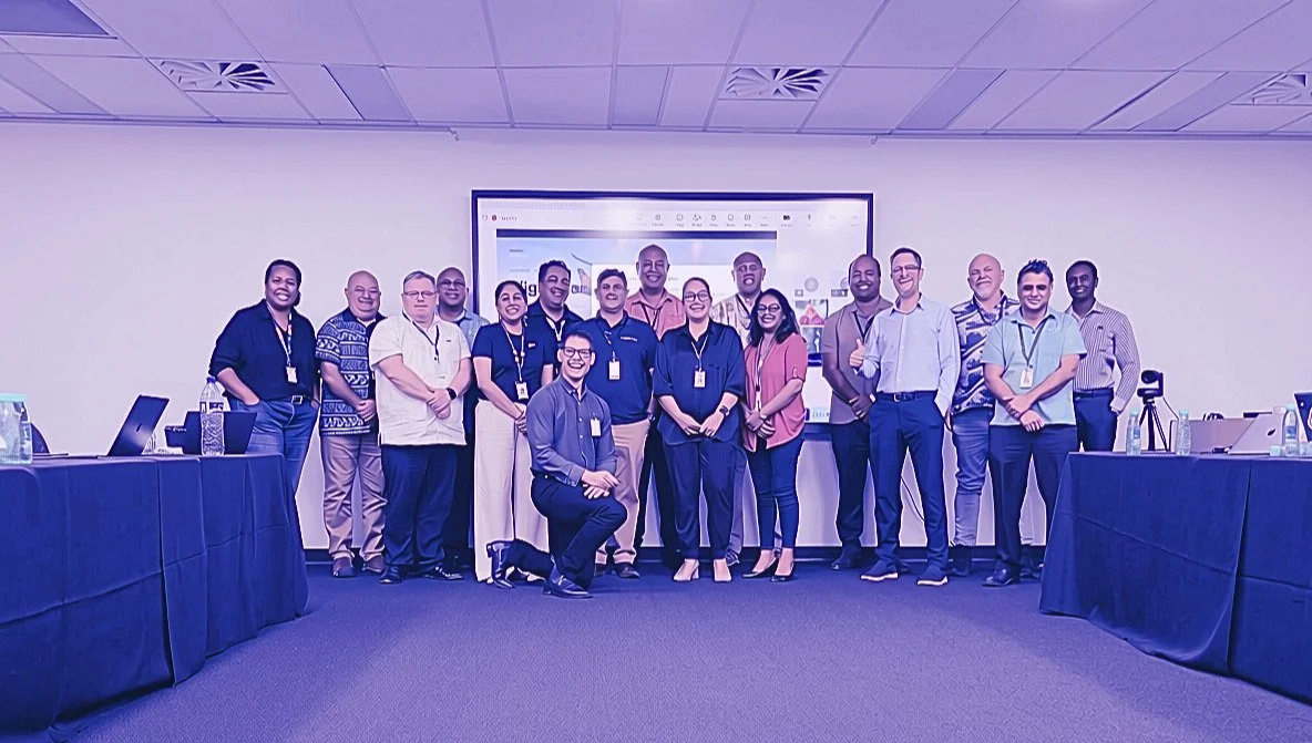 Group of diverse professionals standing in a conference room, posing for a photo in front of a large display screen.