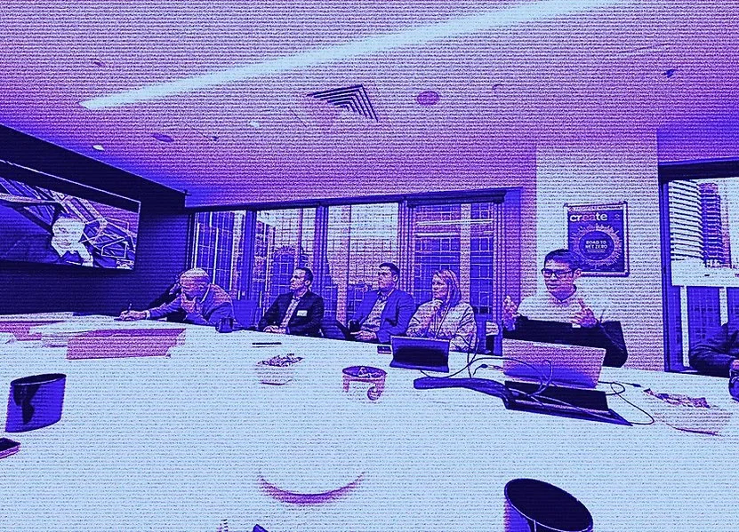 Chieftns.ai Chief AI Officer presenting in a boardroom setting, to people sitting at a conference table during a meeting in a modern office, with large windows and cityscape view outside.