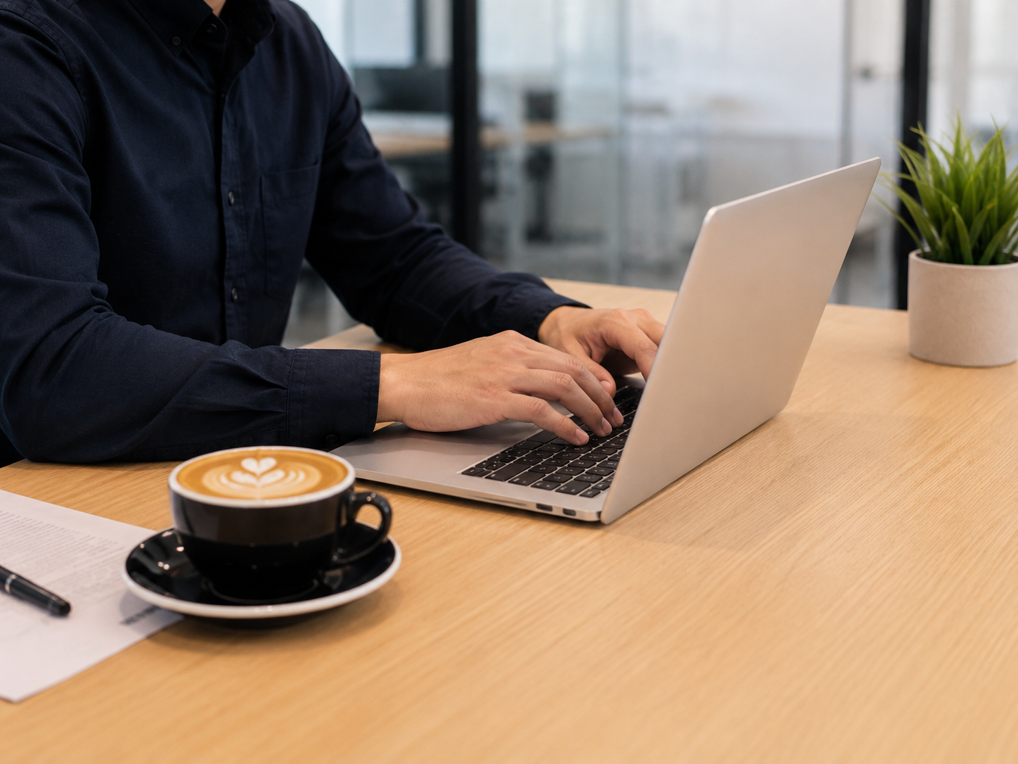 A person sitting at a laptop doing work in a corporate environment with a great looking coffee