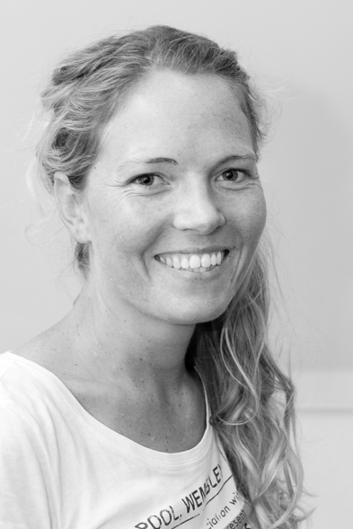 Black and white portrait of a smiling woman with long, wavy hair wearing a t-shirt.