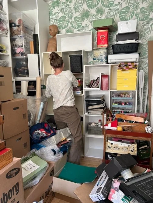 A person organizing or cleaning a cluttered storage room filled with shelves, boxes, and various miscellaneous items.