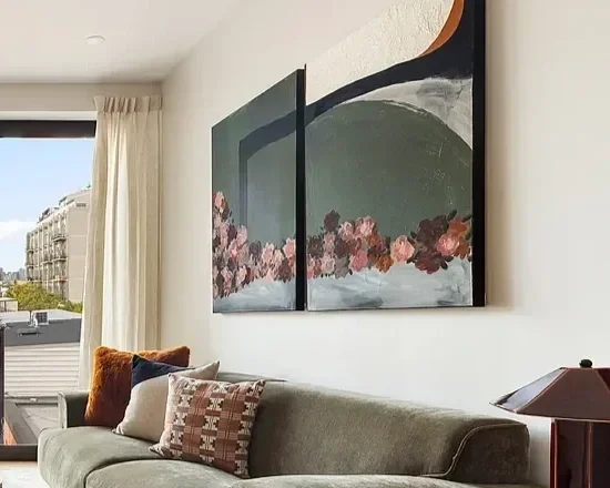 Living room with a large abstract painting on the wall, a gray sofa with patterned and plain pillows, and a window with beige curtains