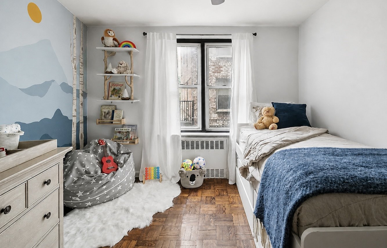 A small bedroom with a window, a bed with a teddy bear, a plush cloud-shaped chair with a guitar, a dresser, and wall shelves with toys and books. There is a painted blue mural on the wall and a white fluffy rug on the wooden floor.