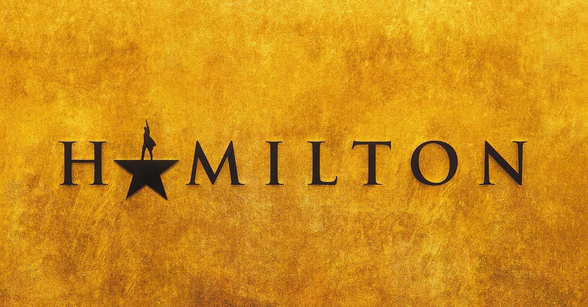 Decorative sign with the word "HAMILTON" in black letters on a gold textured background, featuring a star with a small figure standing on top of it at the start of the word.