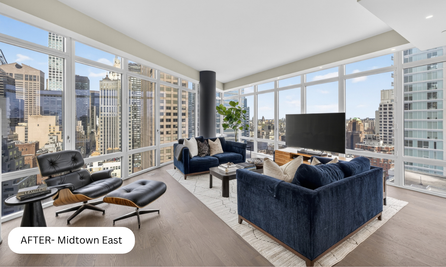 Modern living room with large windows showing city skyline, blue velvet sofas, black lounge chair, wooden coffee table, TV, and indoor plant.