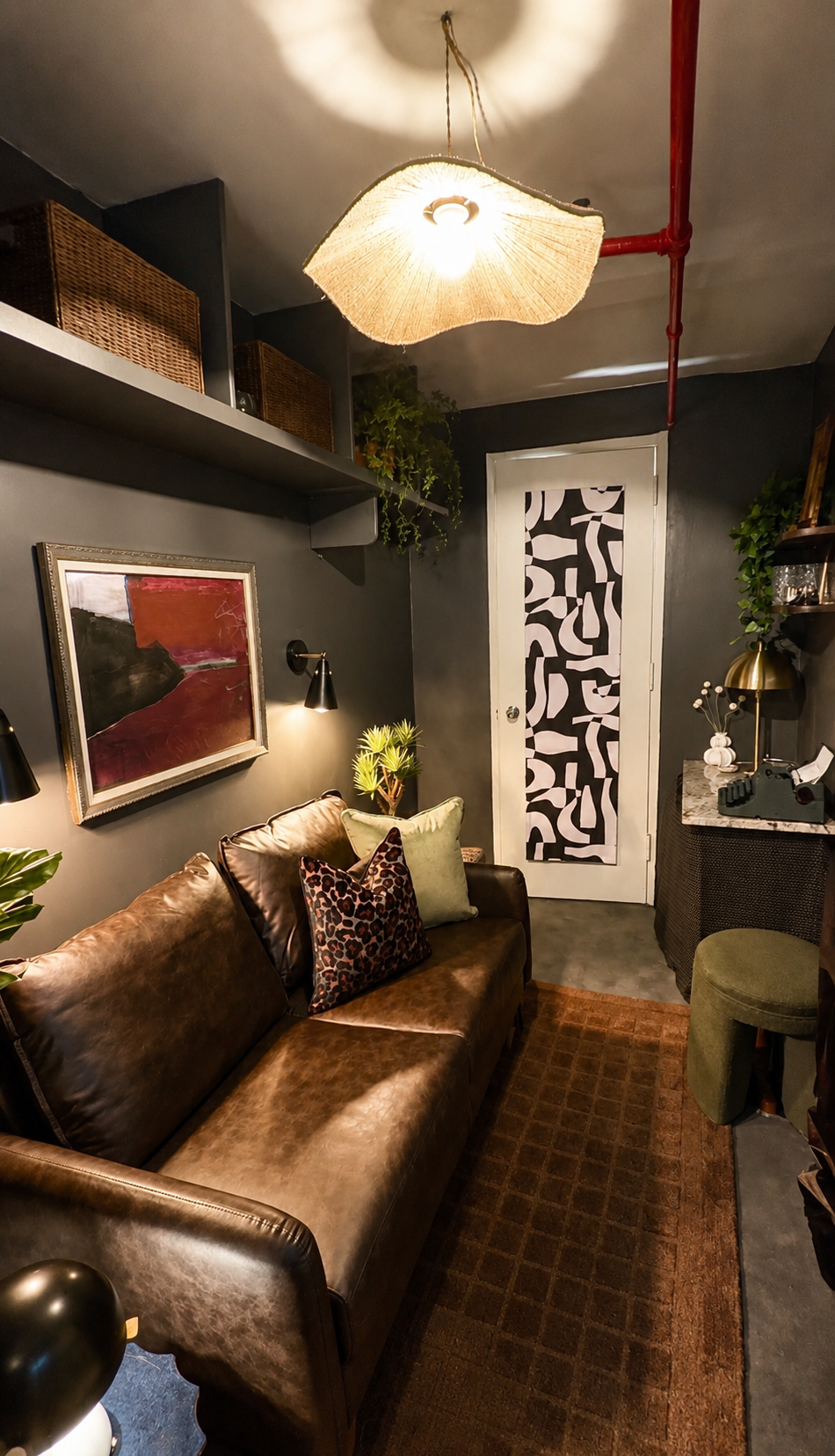 A cozy living room with a leather sofa, decorative pillows, wall art, wall sconces, plants, a patterned door, and a ceiling light fixture.