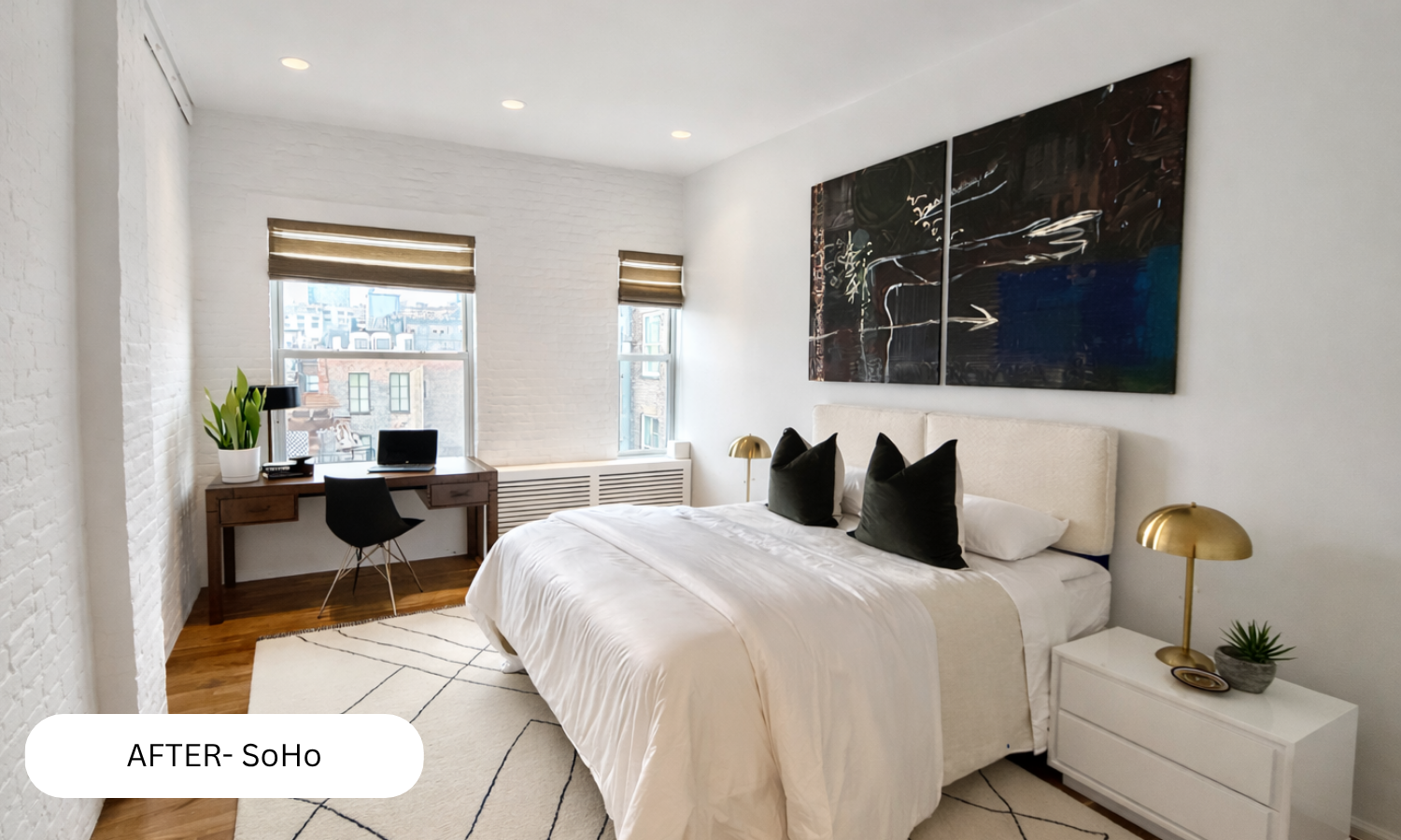 Modern bedroom with white brick walls, a large bed with black pillows, abstract artwork above the bed, a white nightstand with a gold lamp and small plant, and a wooden desk with a lamp, laptop, and plant near windows with city views.