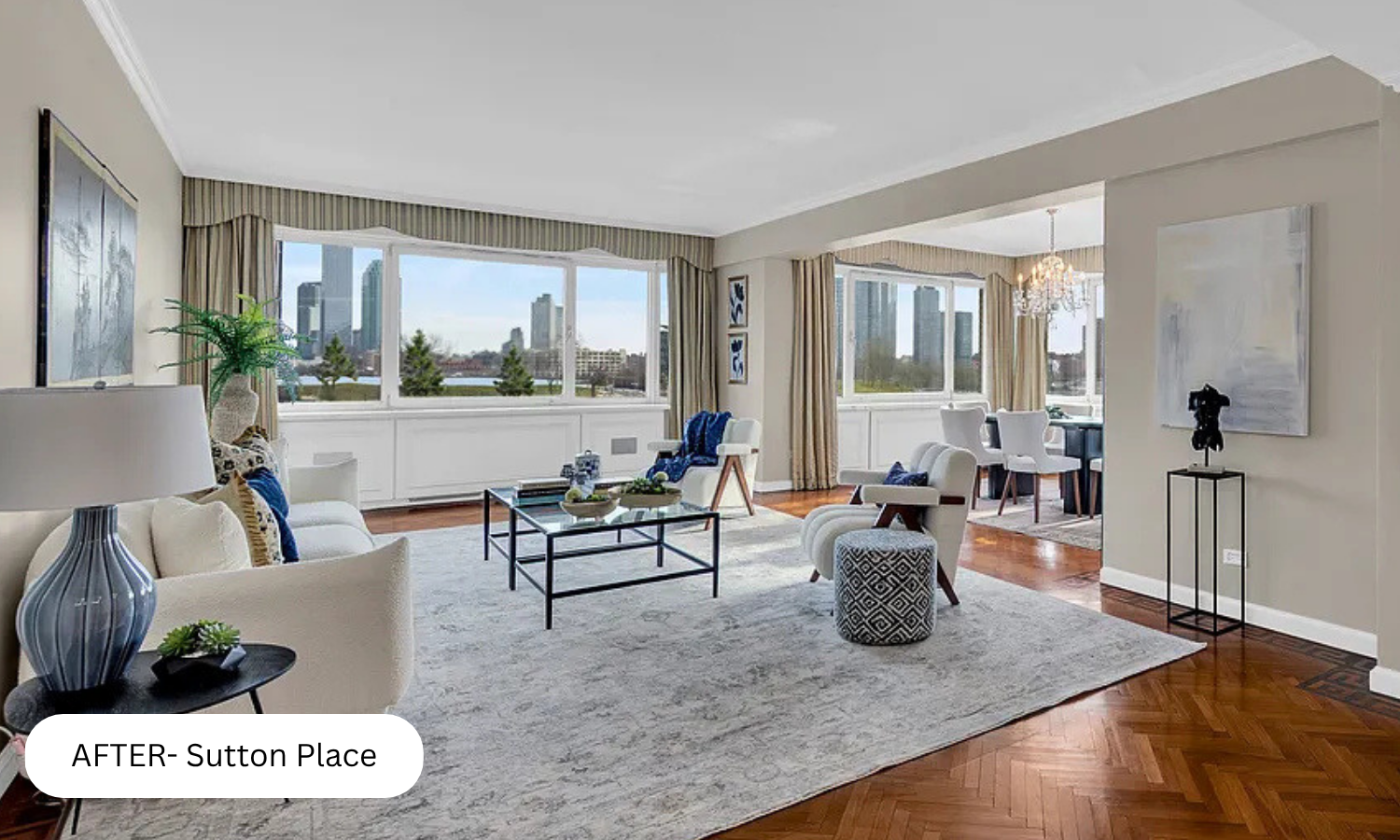 Bright living room with large windows showing city skyline, beige walls, white and gray furniture, wooden floors, and contemporary decor.