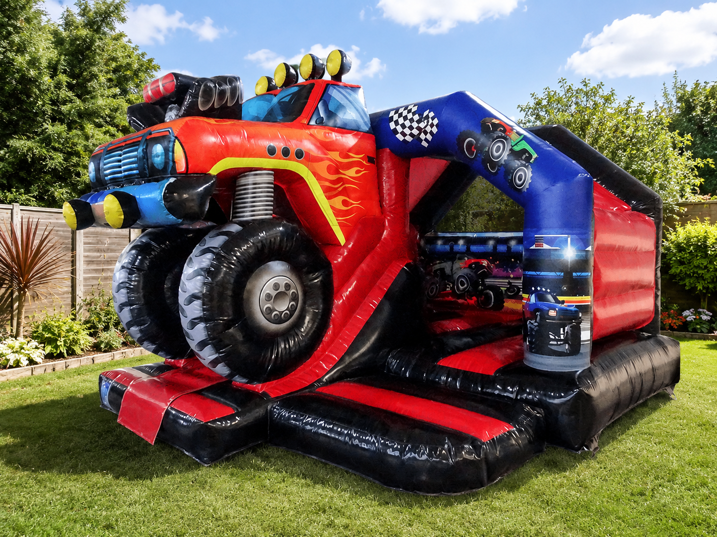 Colorful inflatable bounce house designed like a race car, situated in a backyard with green grass, trees, and a wooden fence, under a blue sky with white clouds.