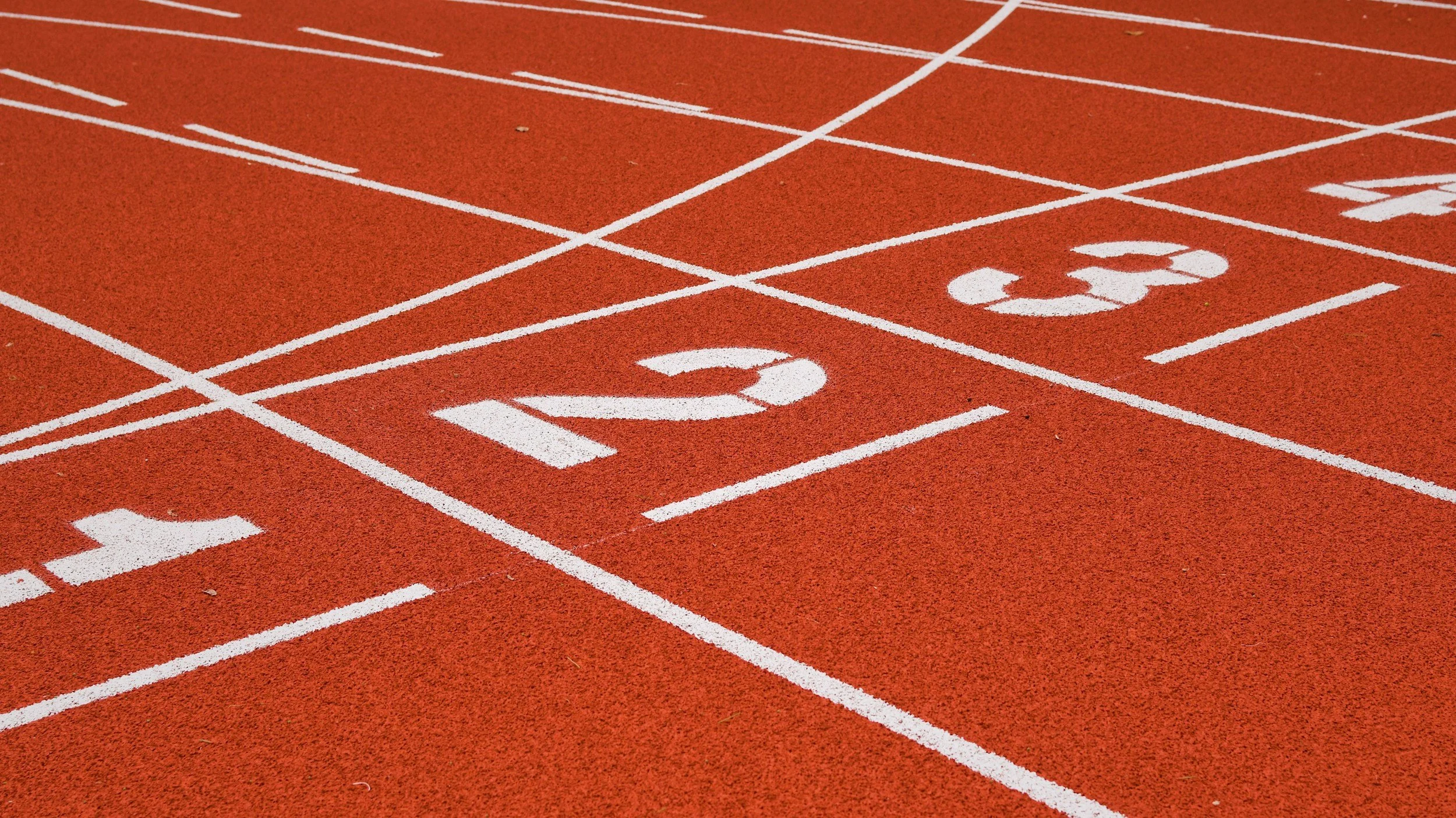 Close-up of a red running track showing lanes numbered 2 and 3, with white lane markings.