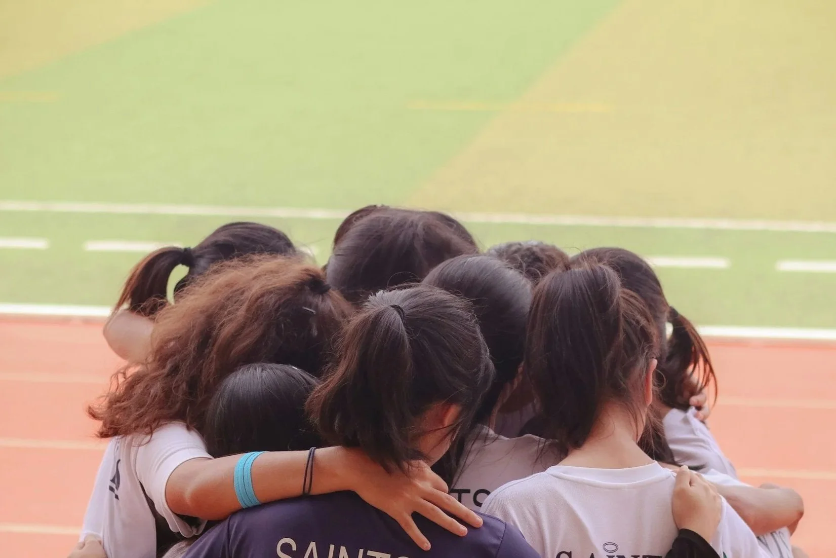 Group of young women huddled together in a team hug on an outdoor sports court.