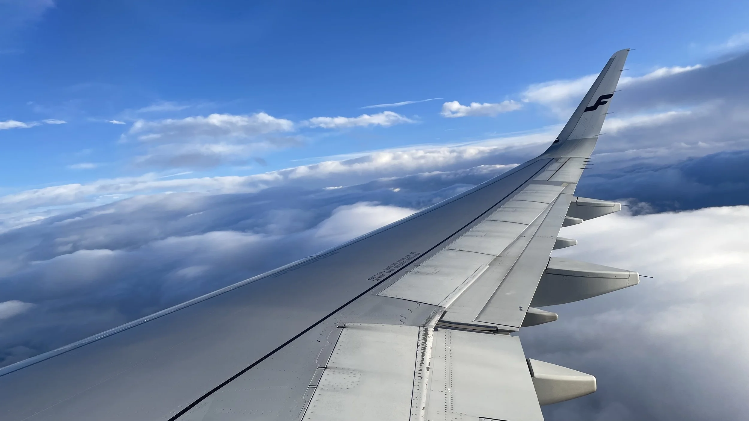View of an airplane wing flying above clouds with a blue sky.