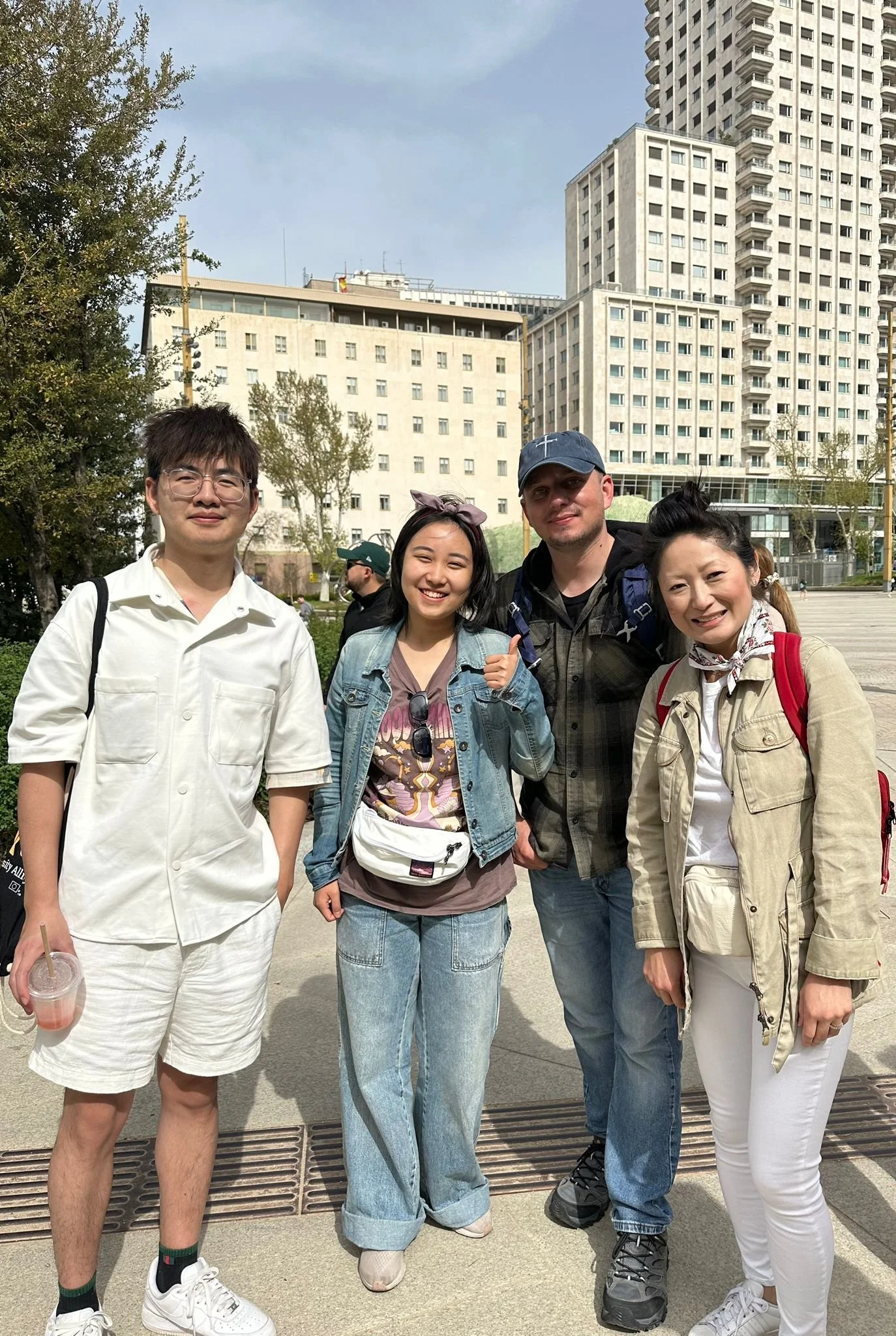 Five people standing outdoors in an urban park, with tall buildings behind them, smiling and posing for the photo.