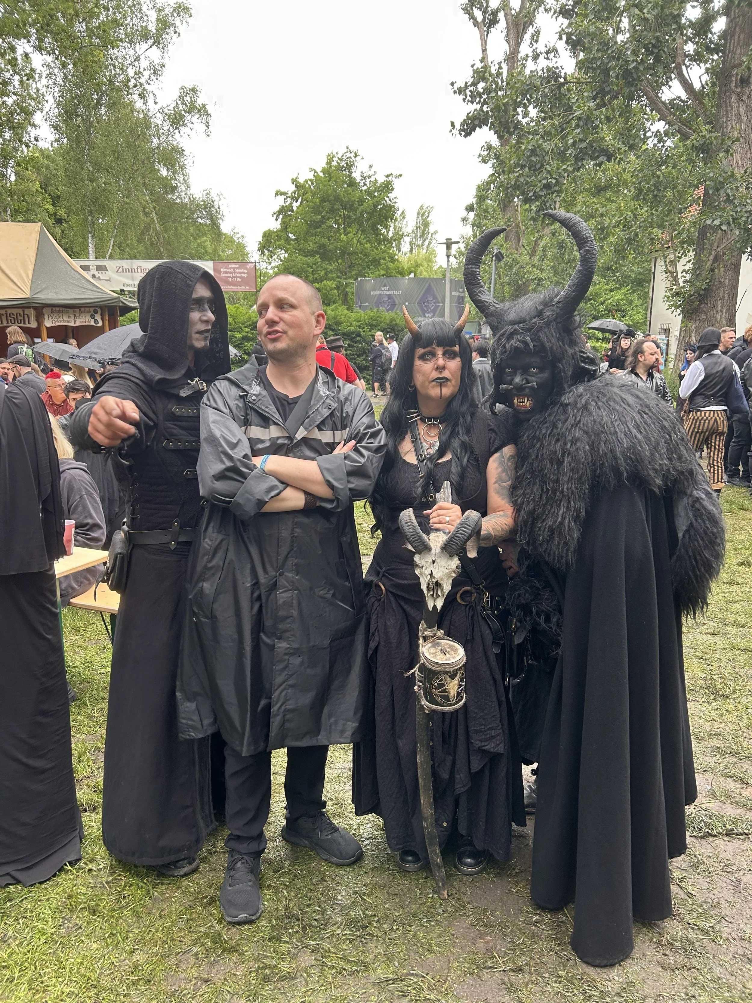 People dressed in costumes, including one with horns and another with face makeup, gathered outdoors during a festival or event.