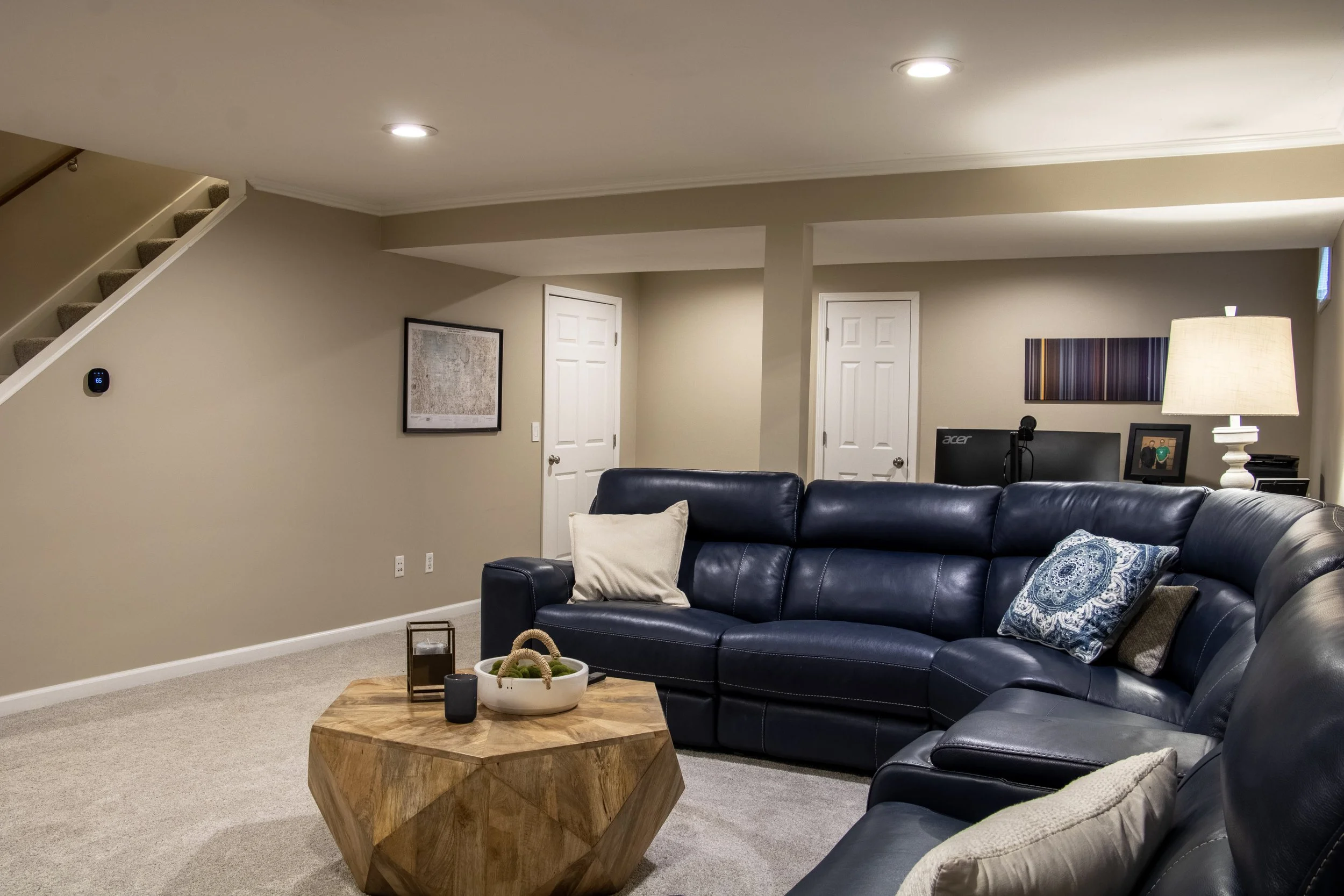 Living room with beige walls, a blue leather sofa and matching chairs, a wooden coffee table with decorative items, wall art, lamp, and electronic devices.